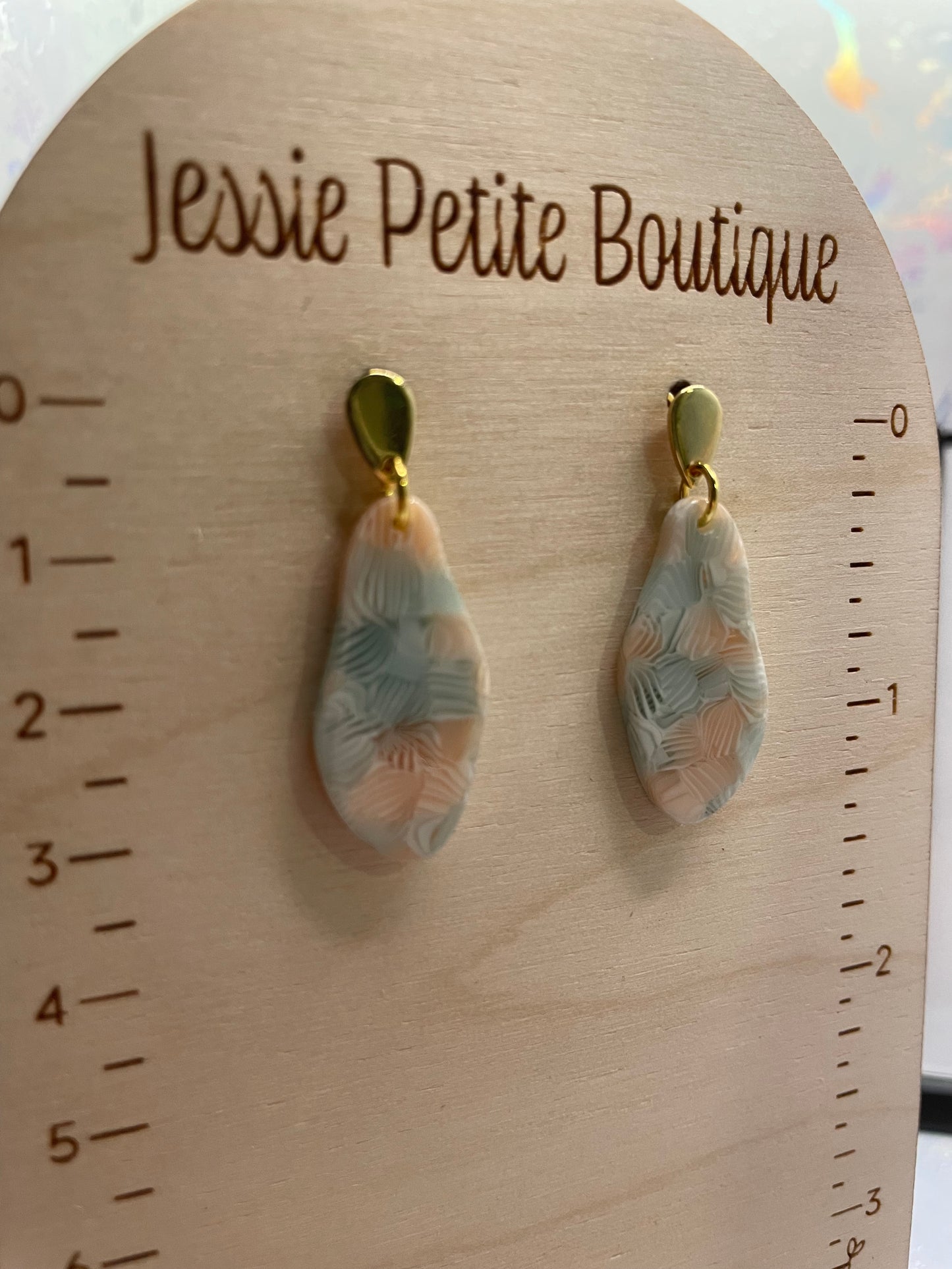 Pair of earrings on a wooden board with 'Jessie Petite Boutique' branding.