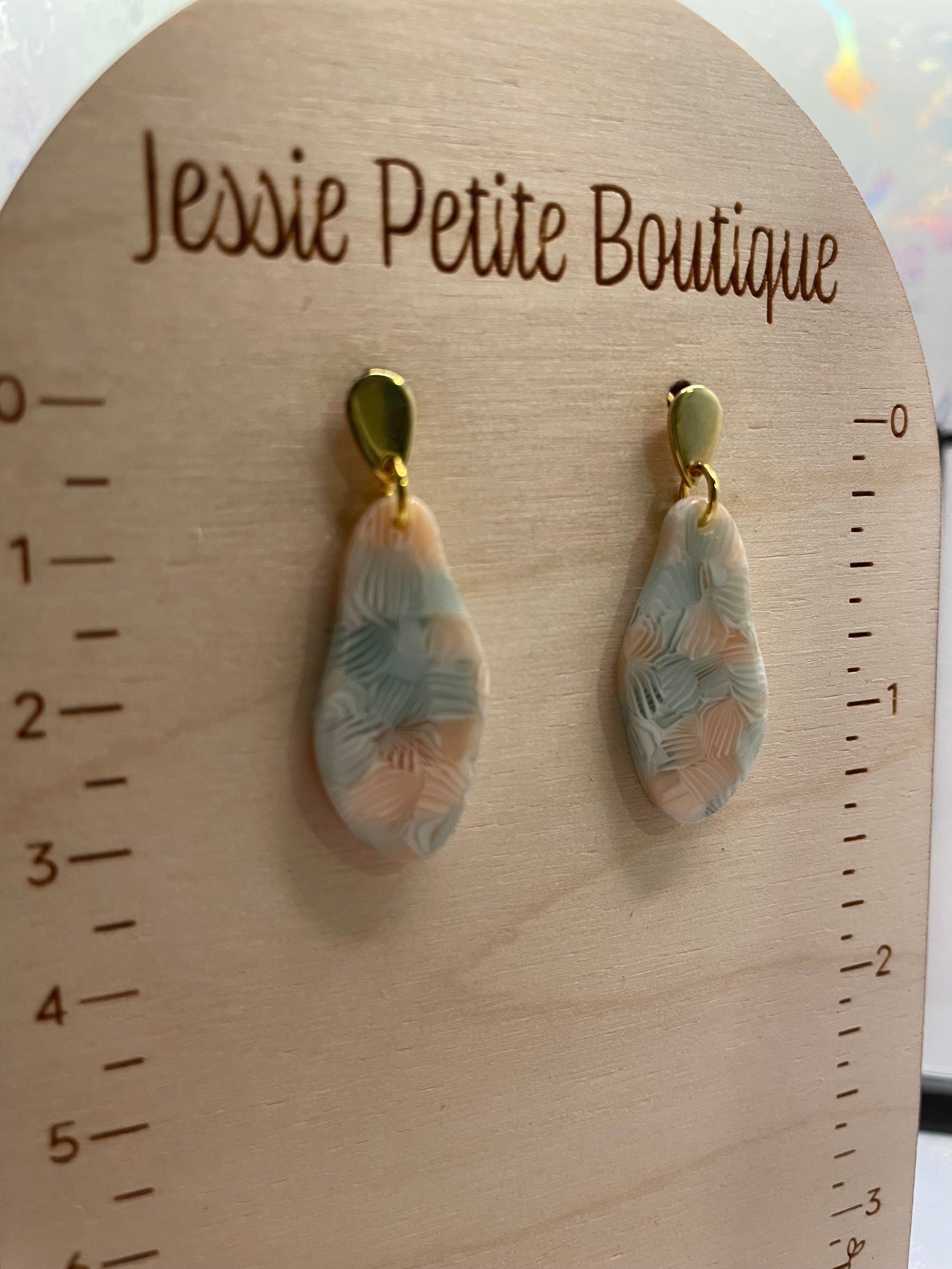 Pair of earrings on a wooden board with 'Jessie Petite Boutique' branding.