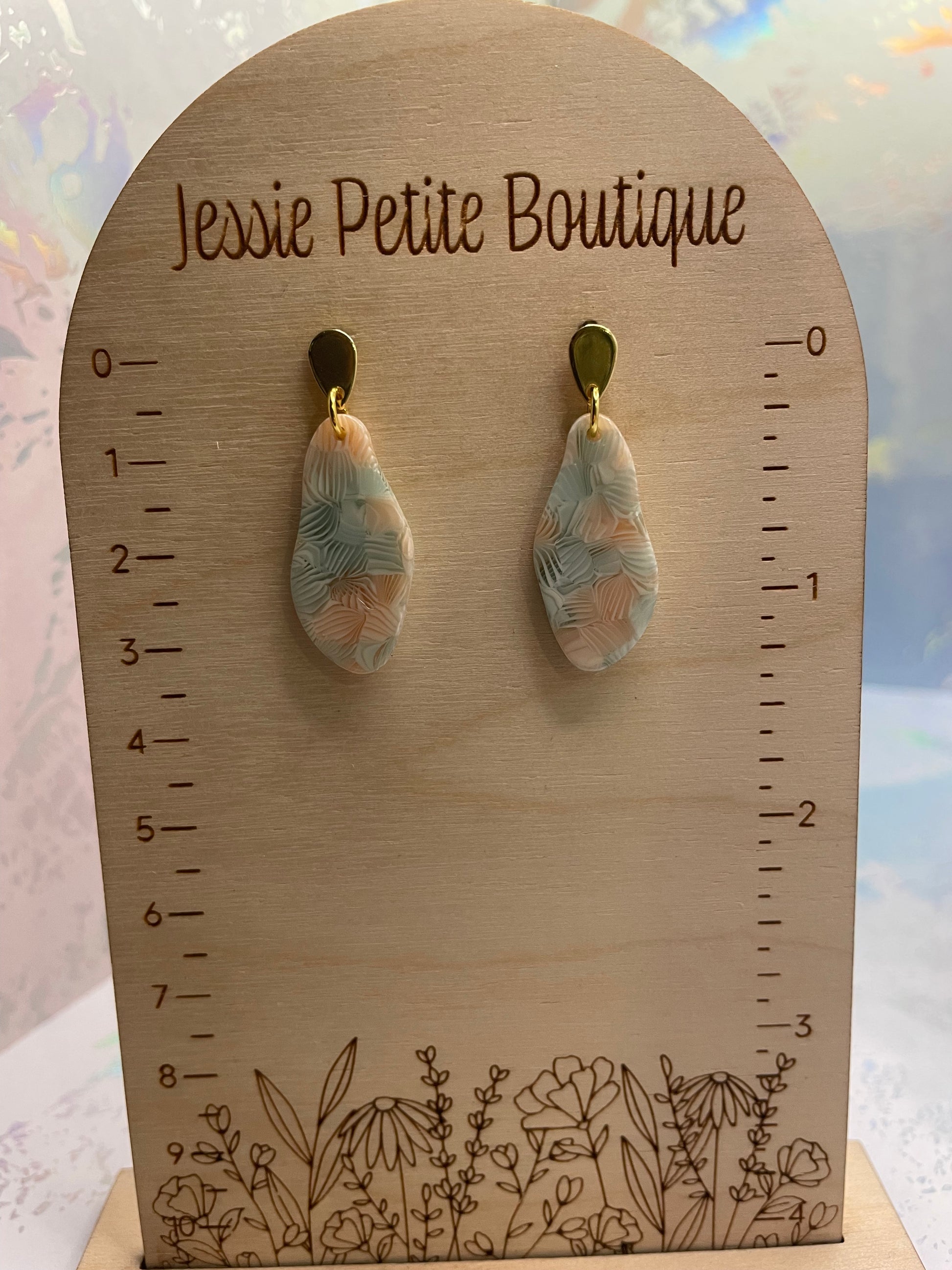 Teardrop-shaped earrings on a wooden card with floral design and 'Jessie Petite Boutique' text.