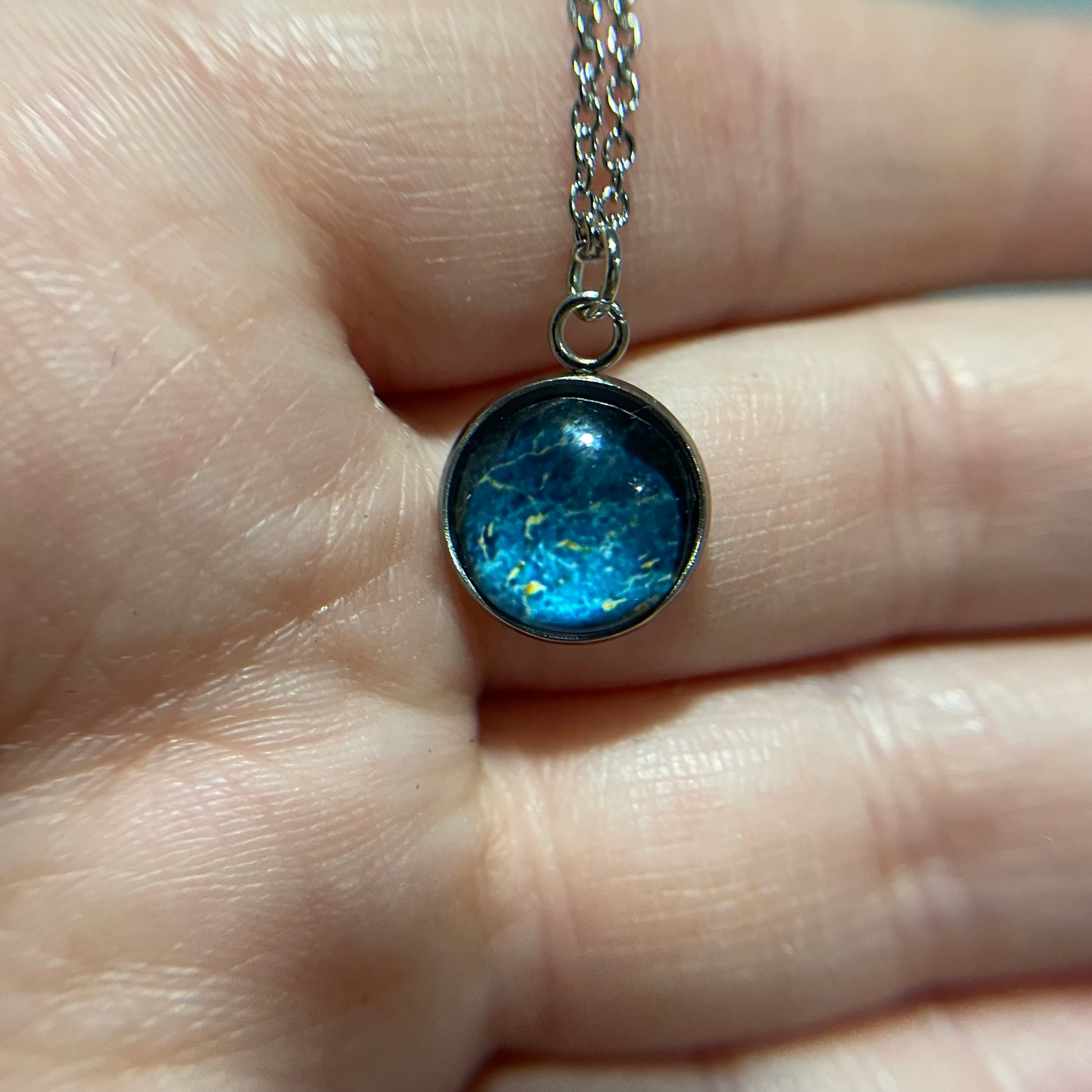 Blue pendant necklace held between fingers