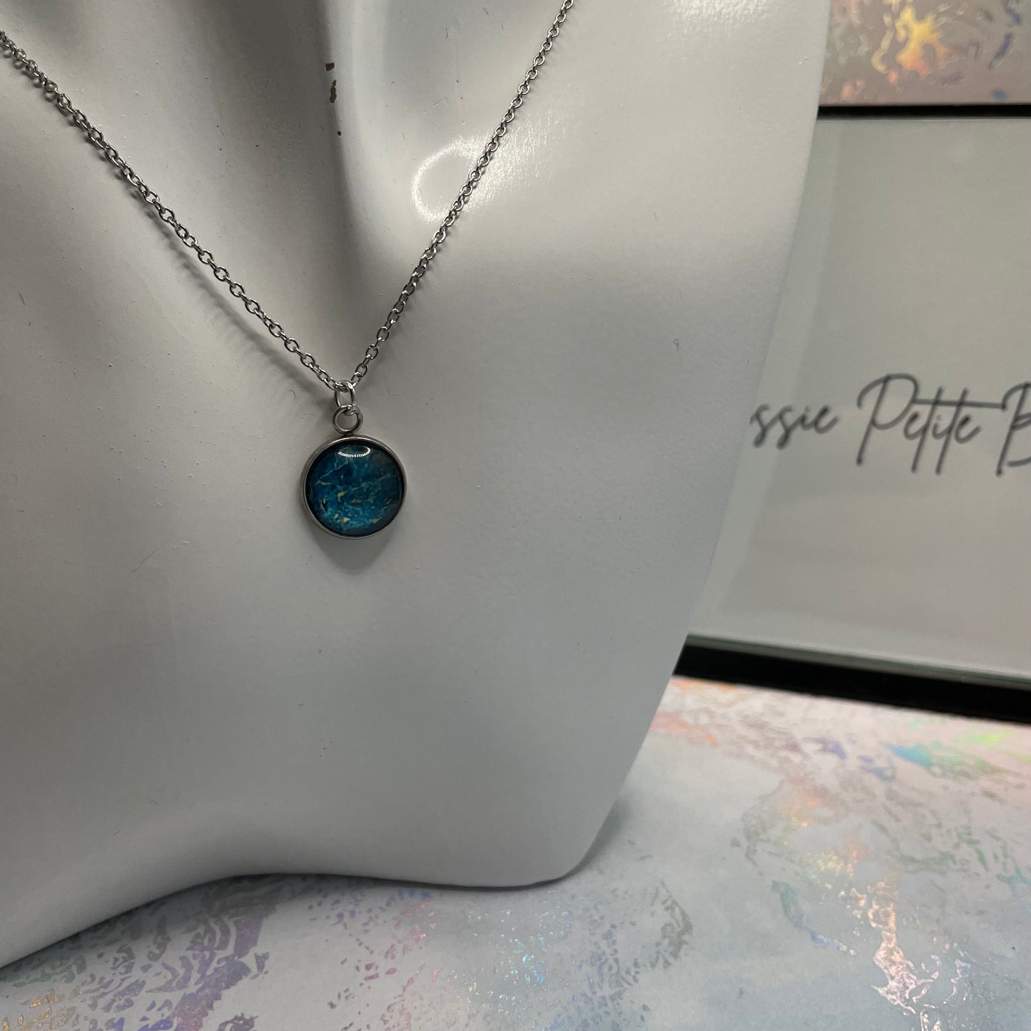 Necklace with a blue pendant on a mannequin bust, with 'Bella' branding in the background.