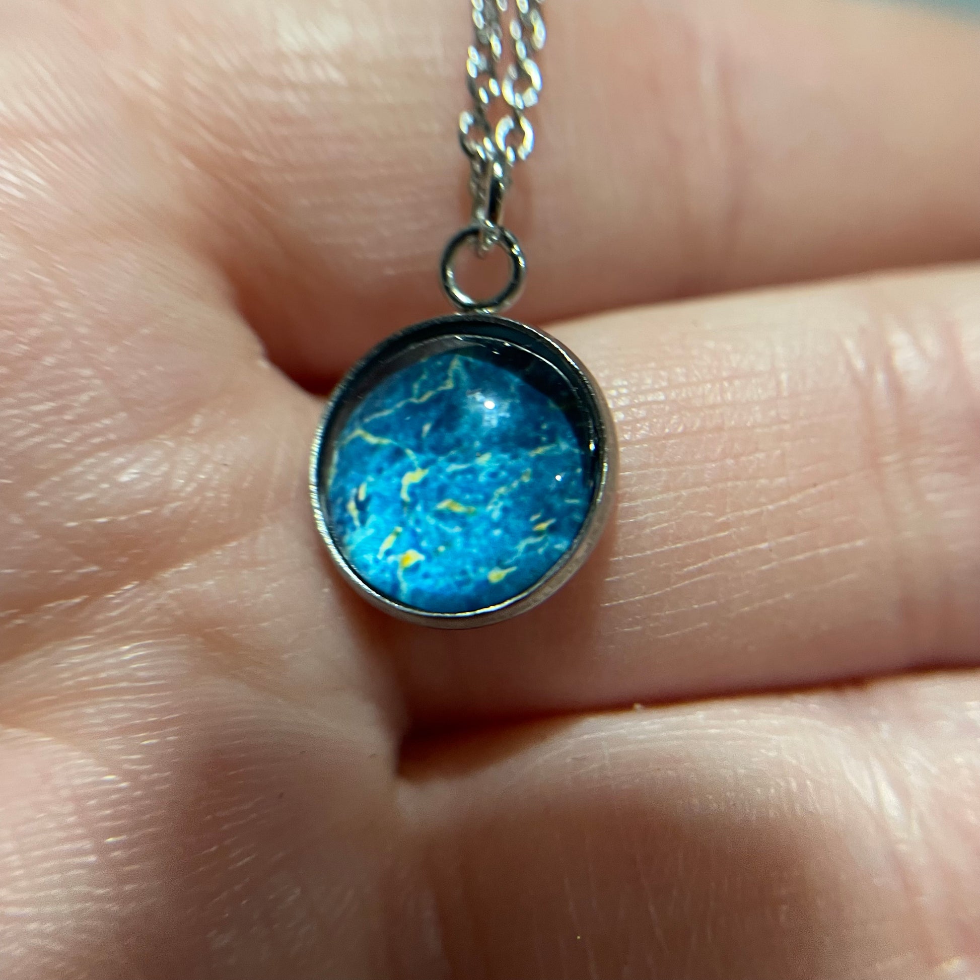 Blue pendant necklace held between fingers