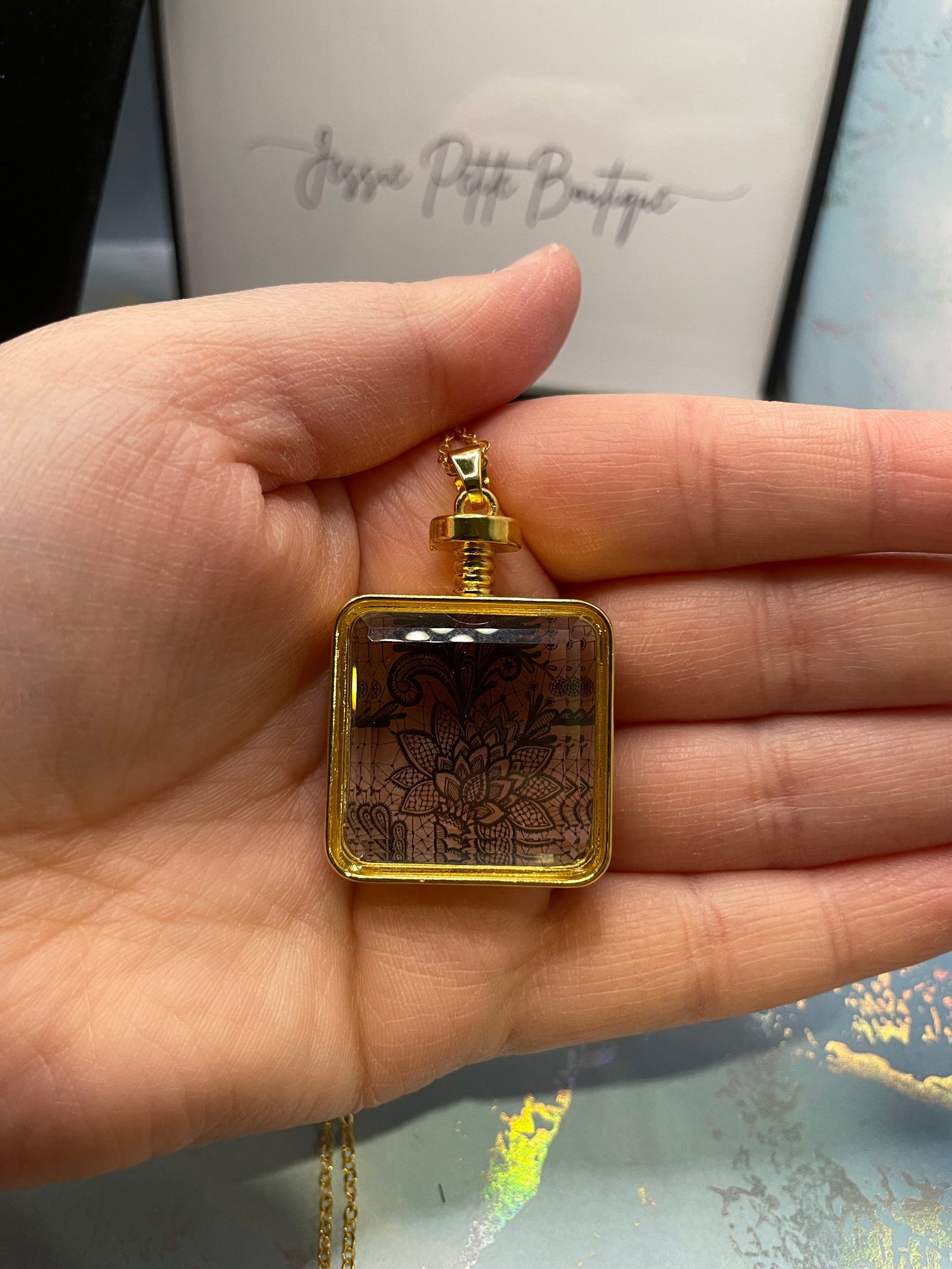Gold necklace with a square pendant held in a hand