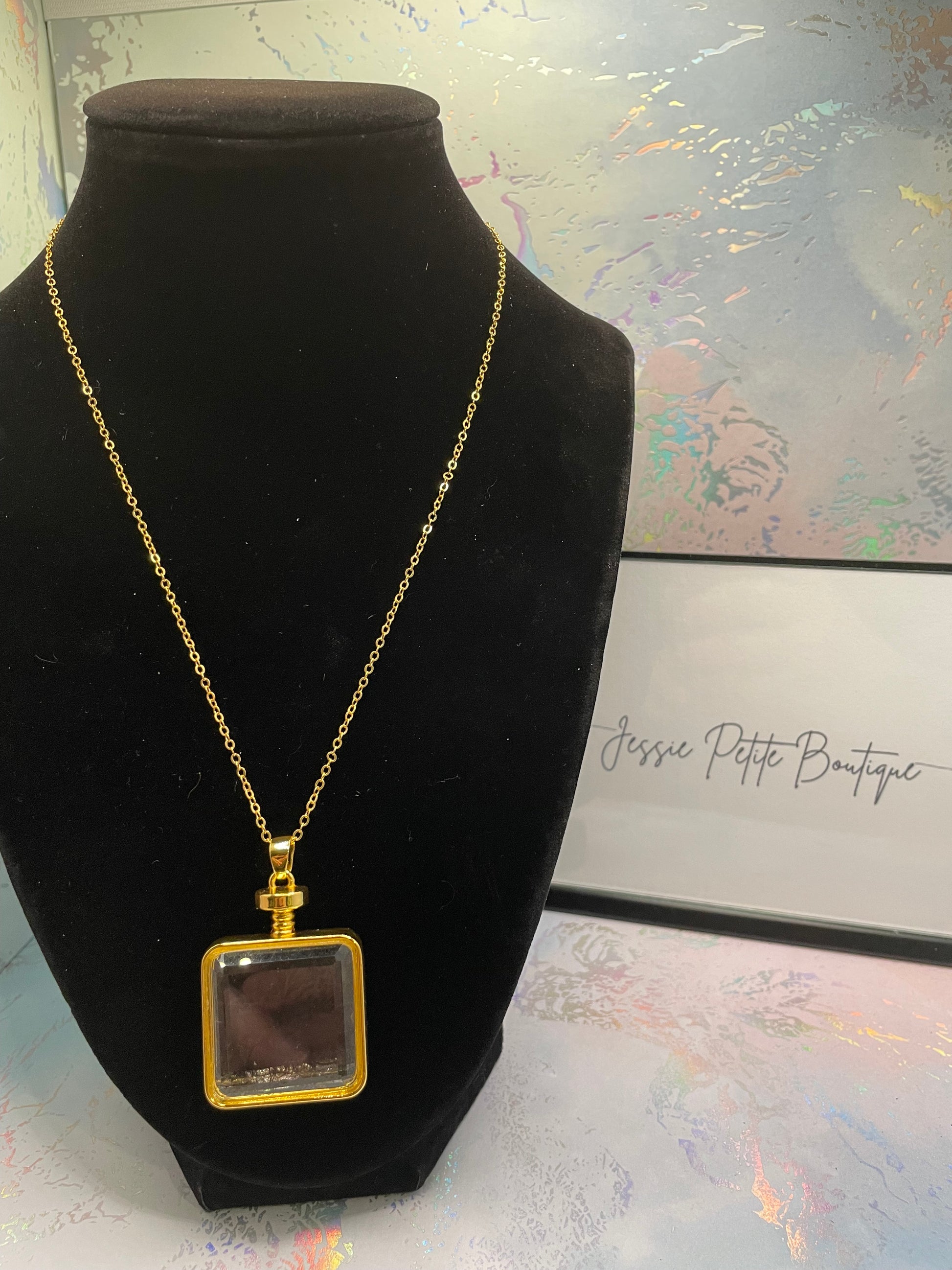 Gold necklace with a square pendant on a black velvet stand against a decorative background