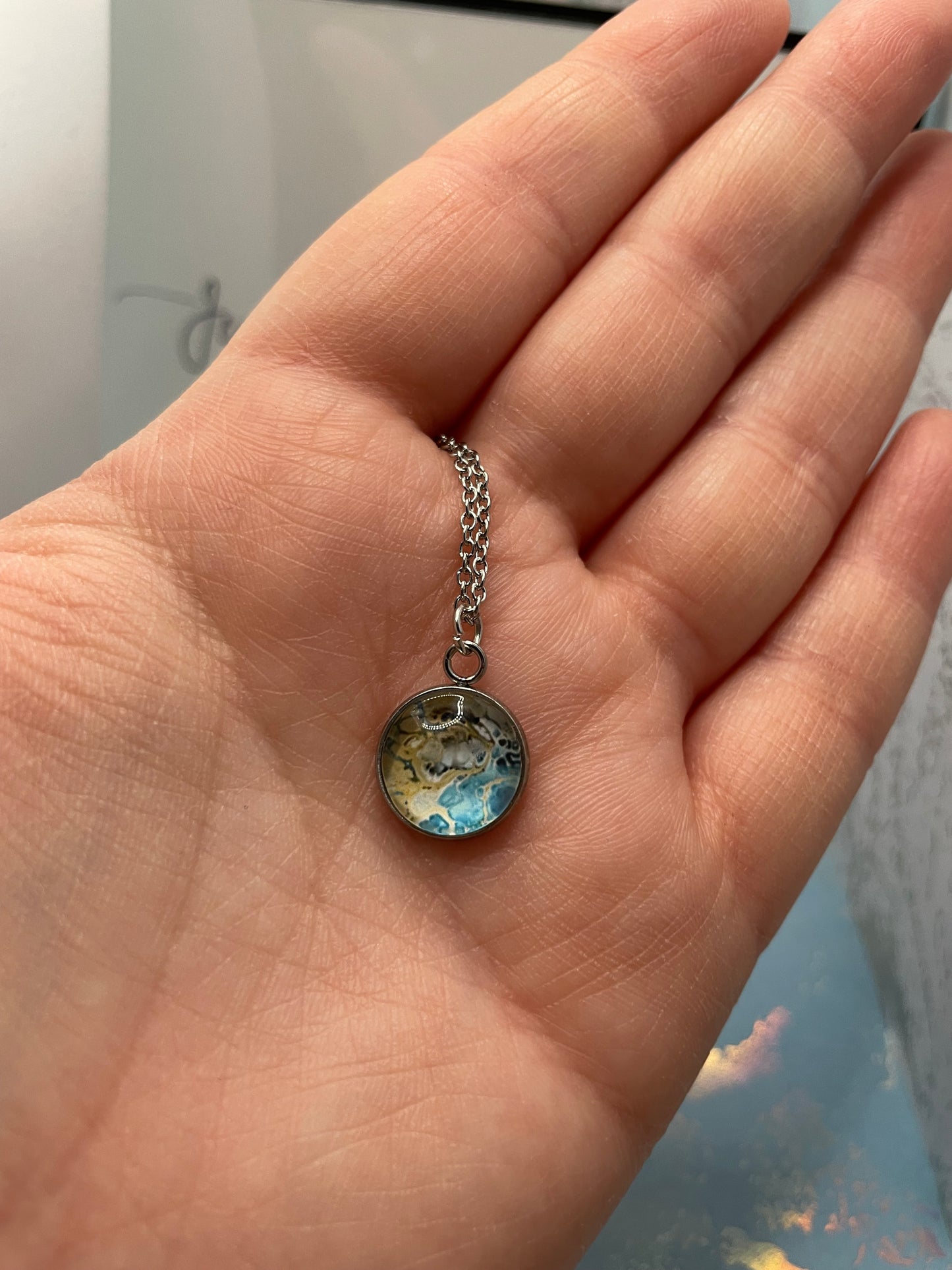 Hand holding a small round pendant with a chain