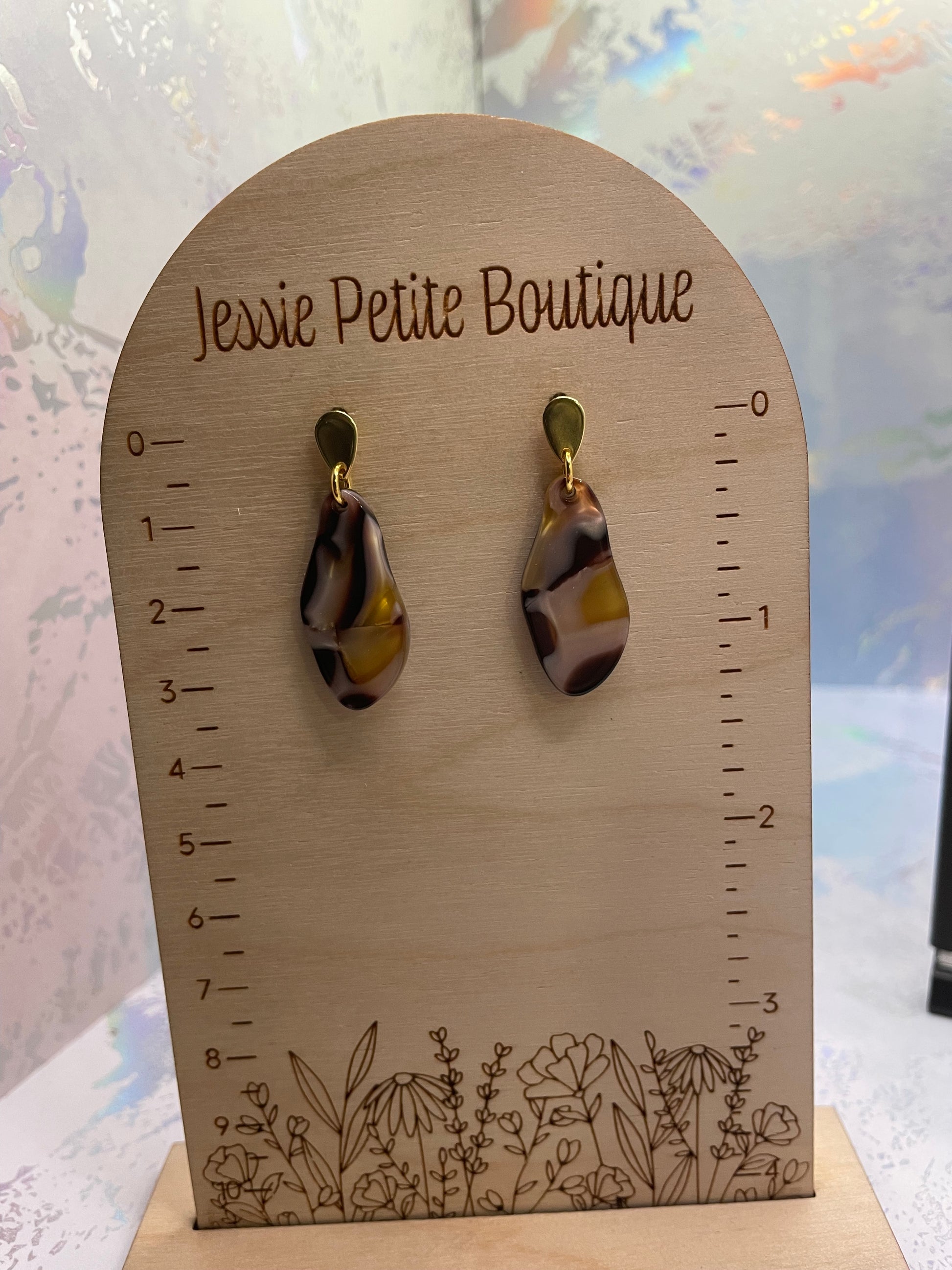 Pair of marbled drop earrings on a wooden card with floral design and measurement scale.