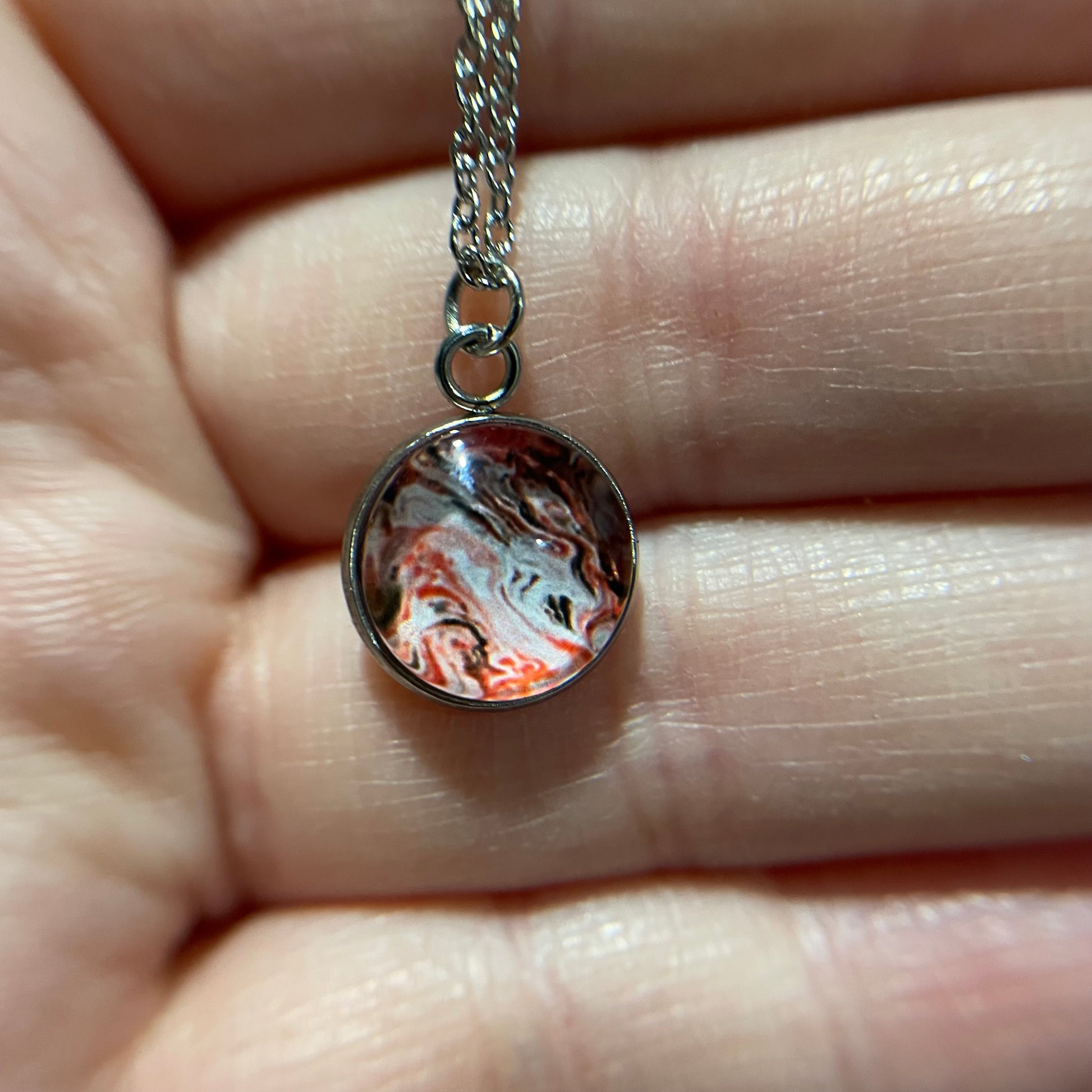 Marble-patterned pendant on a silver chain held between fingers