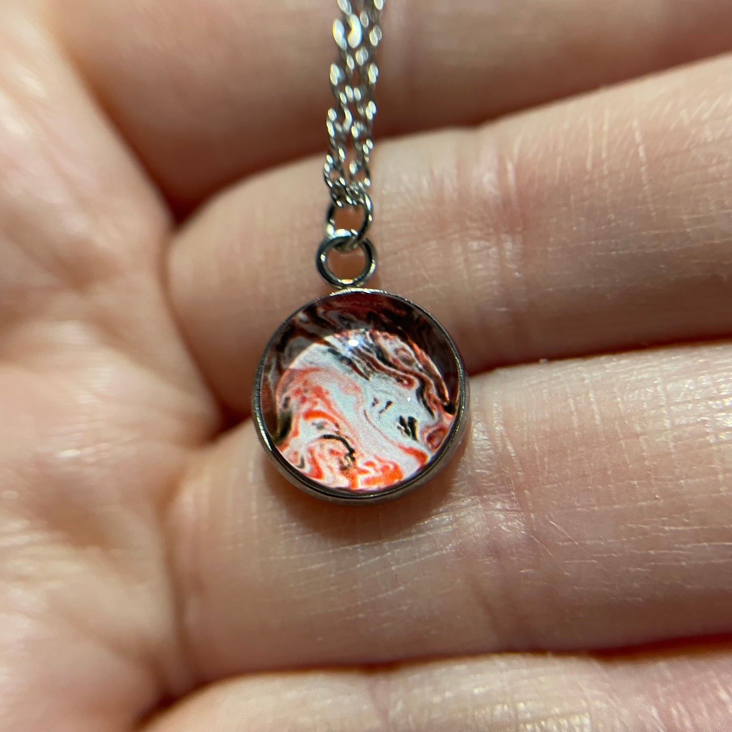 Marbled design pendant on a chain held between fingers