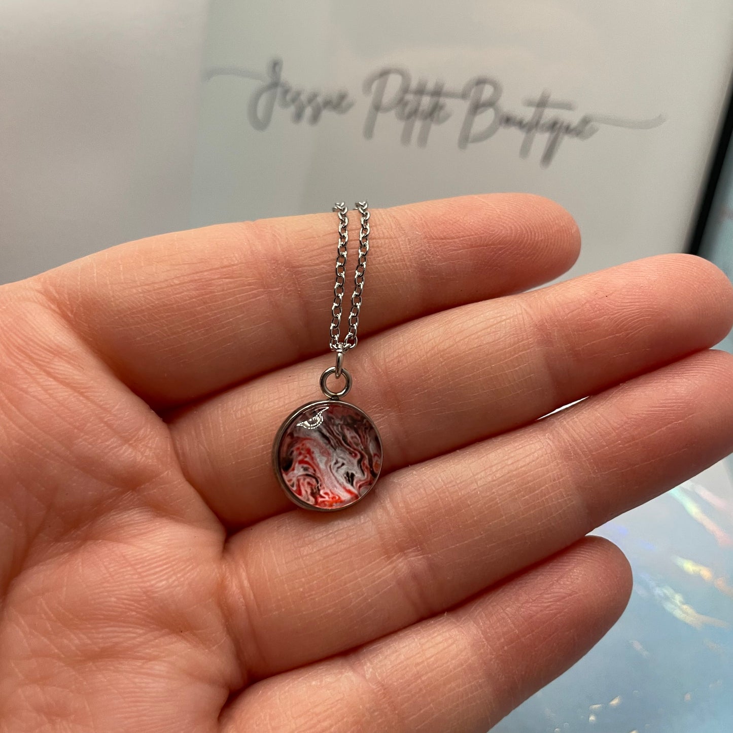 Hand holding a necklace with a round pendant against a branded background