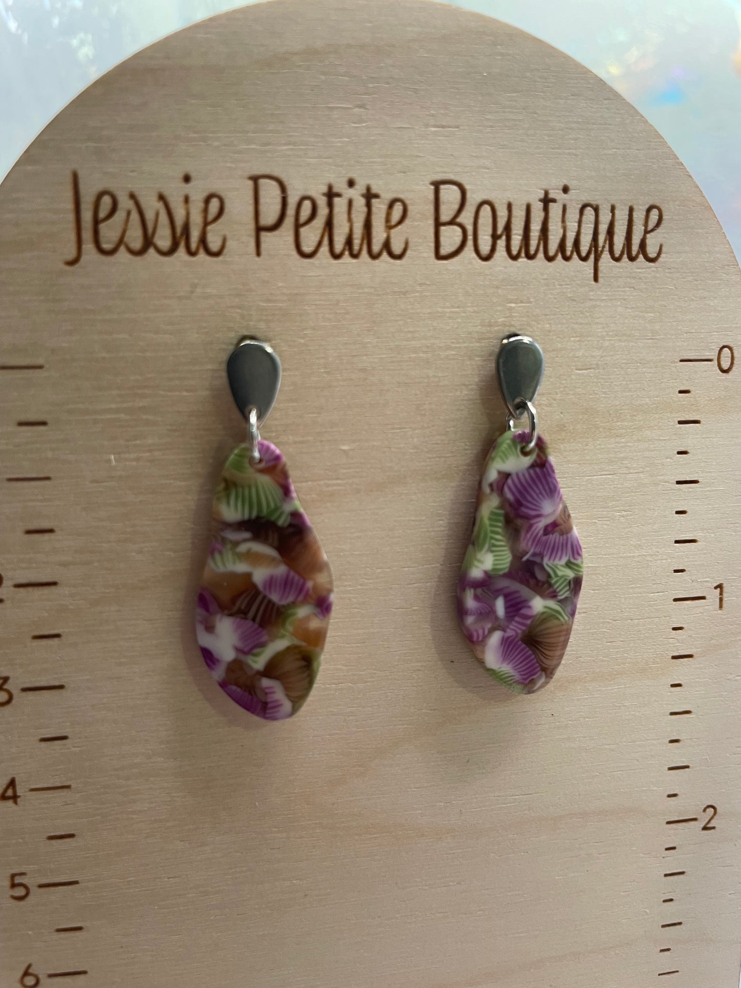 Two patterned earrings on a wooden board with measurement scale and 'Jessie Petite Boutique' branding.