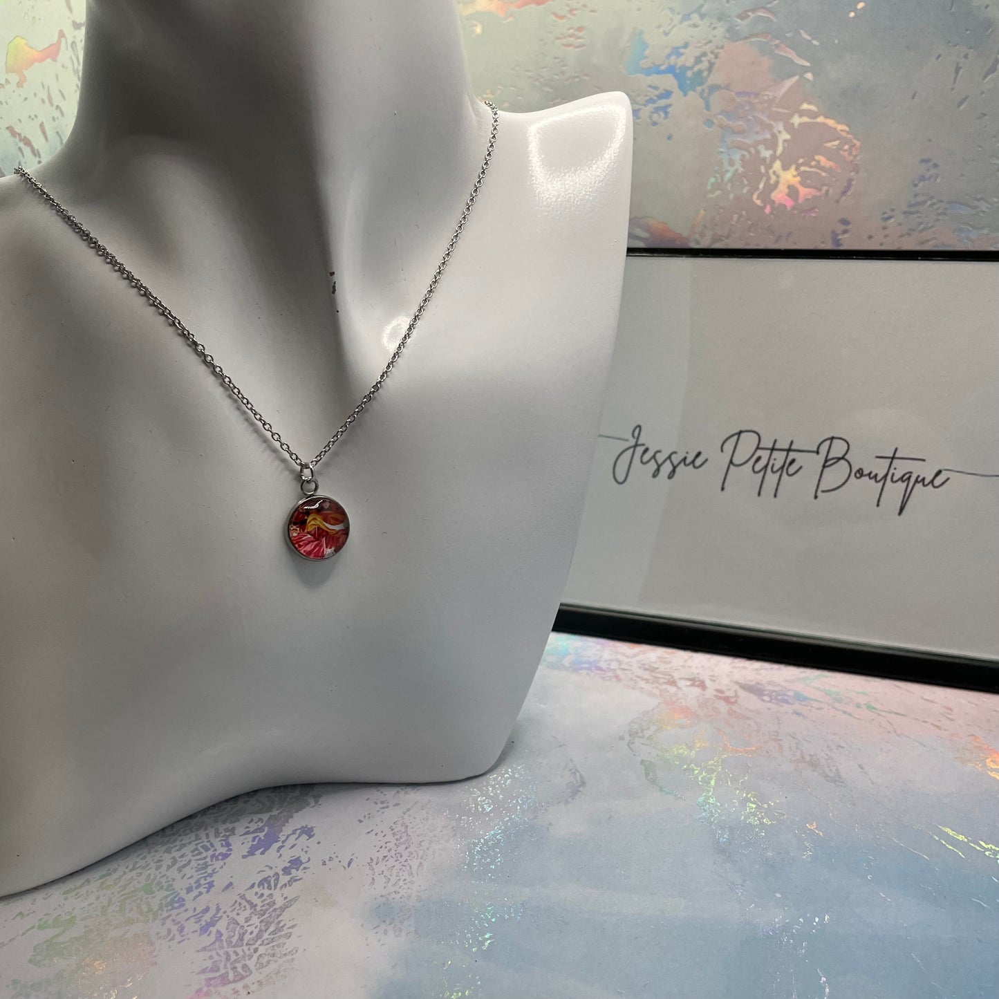 Necklace with a colorful pendant on a mannequin bust in front of a 'Jessie Petite Boutique' sign.