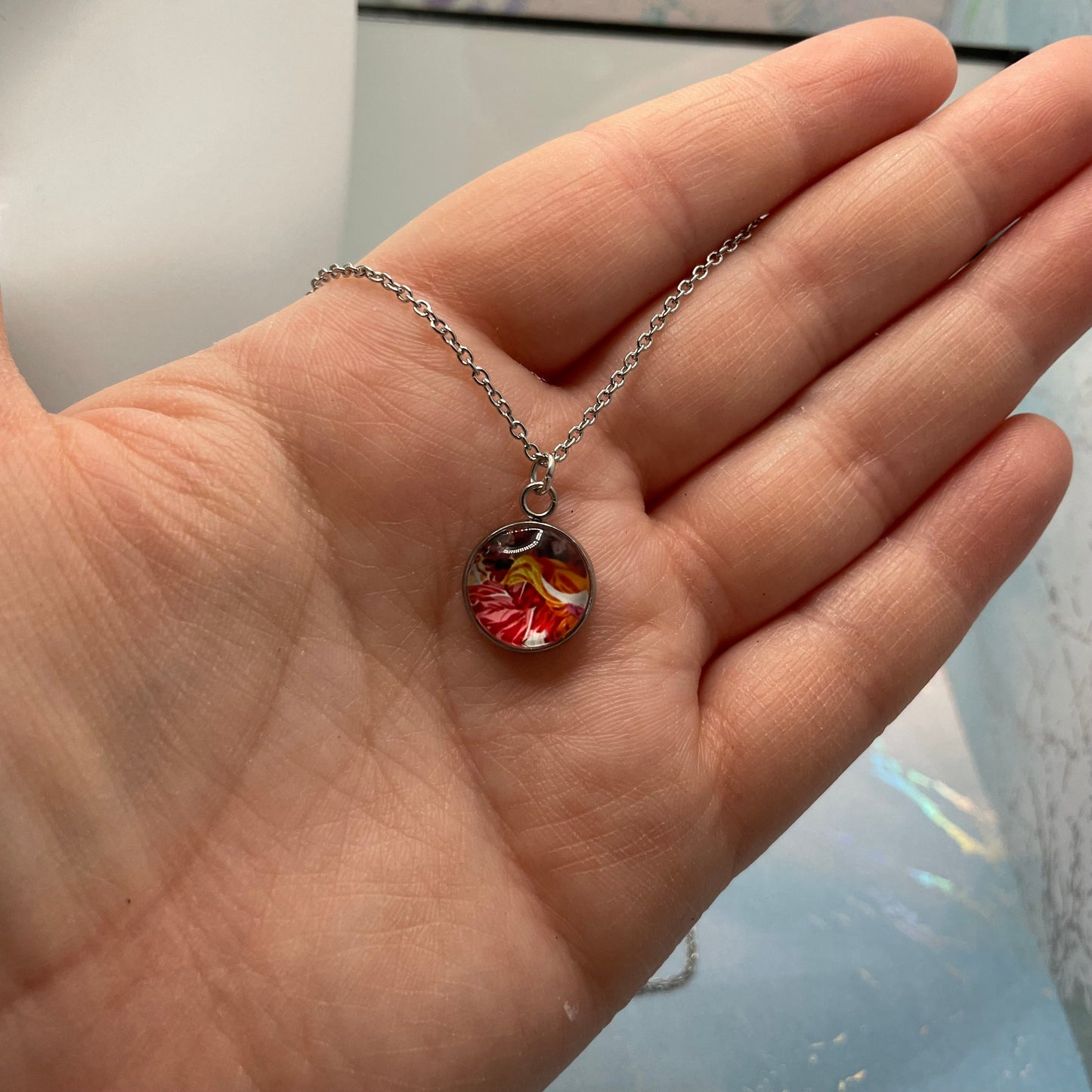 Hand holding a necklace with a floral pendant against a neutral background