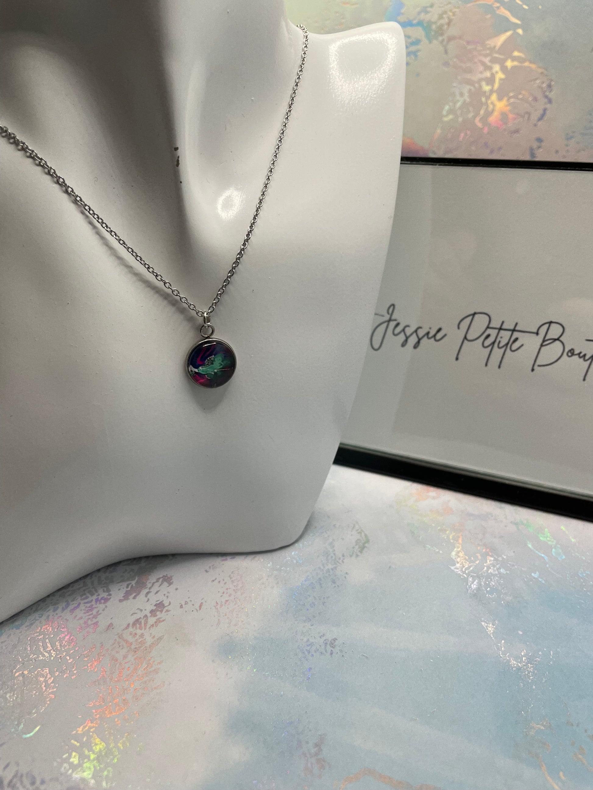 Necklace with a colorful pendant on a mannequin bust against a soft, multicolored background.