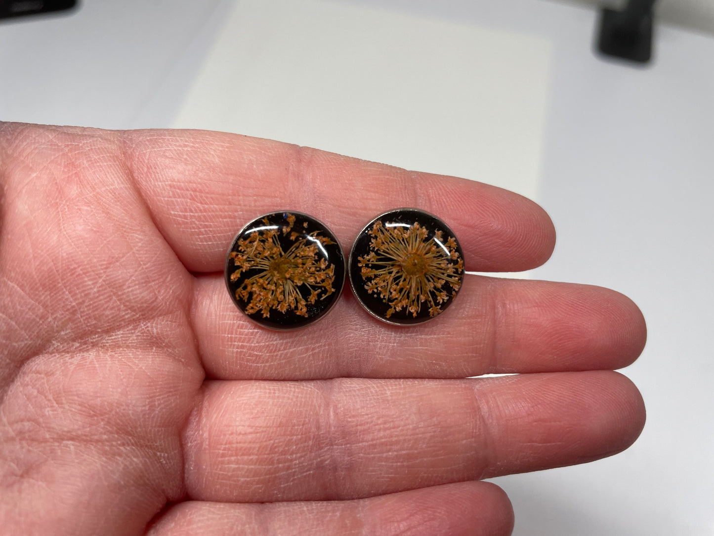 Round earrings with floral design held between fingers on a white background