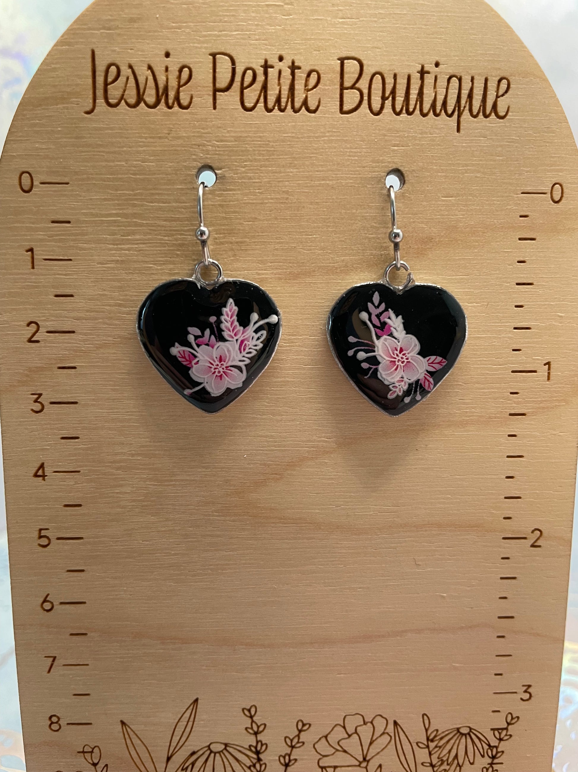 Heart-shaped earrings with floral design on a wooden card with measurement scale and floral designs.