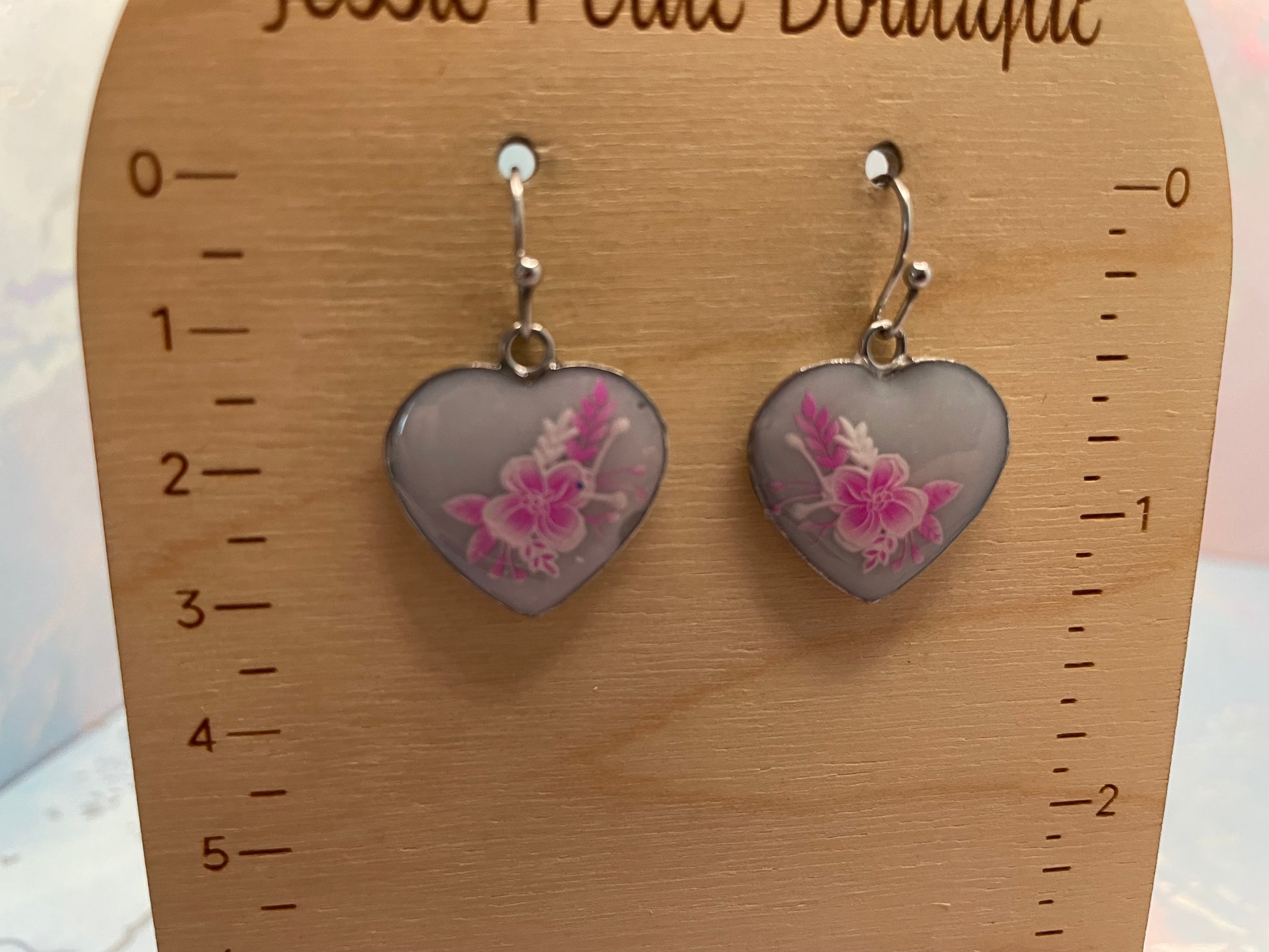 Heart-shaped earrings with floral design on a wooden display card.