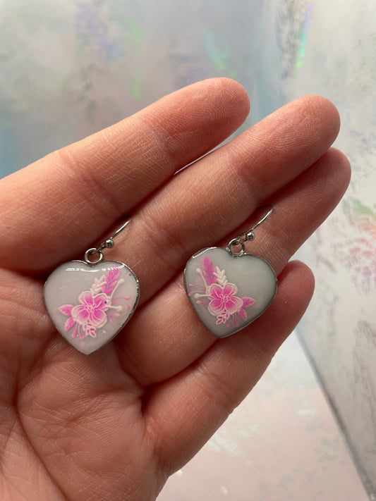 Heart-shaped earrings with floral designs held in a hand against a light background