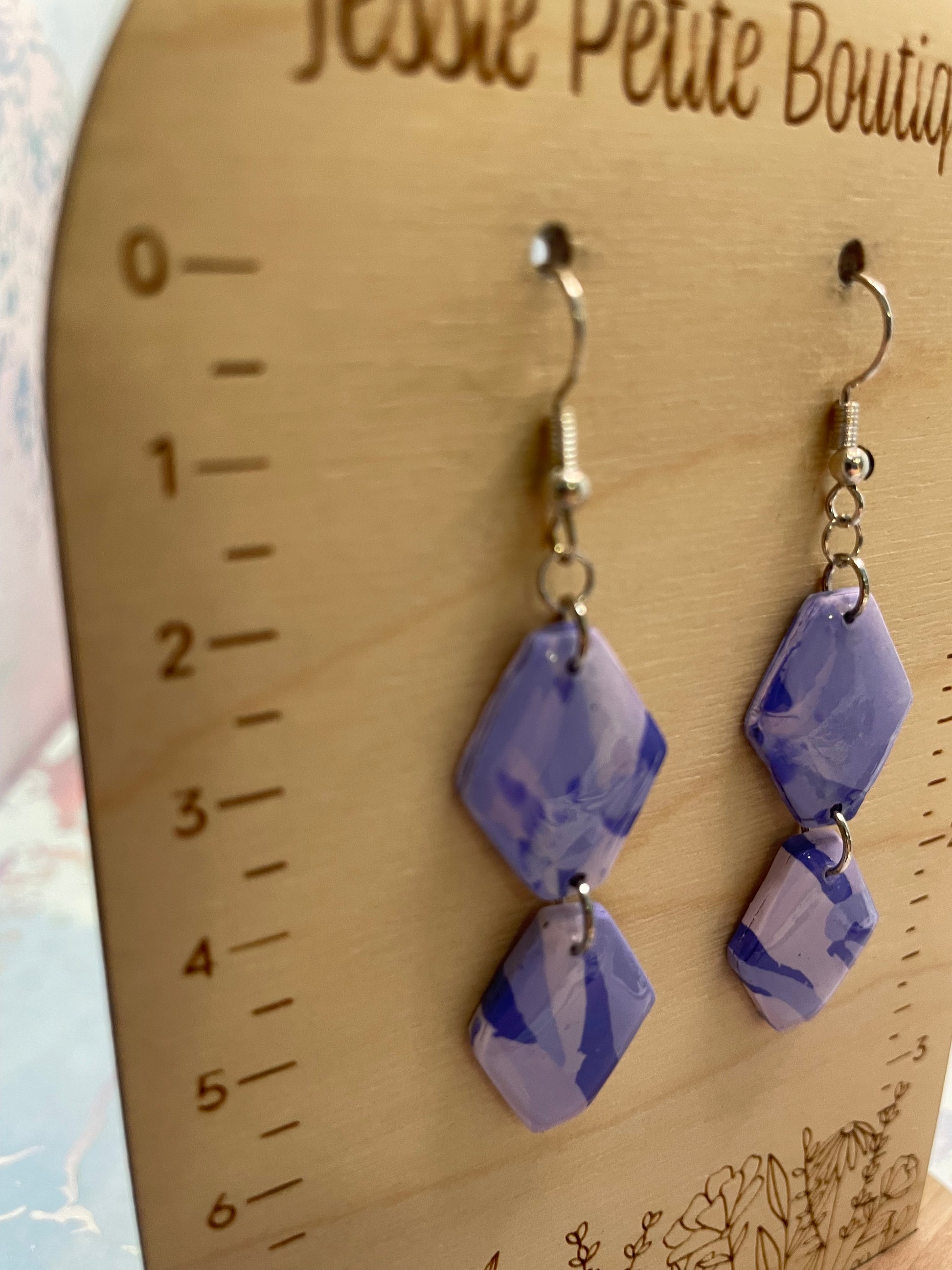 Pair of purple marbled geometric earrings on a wooden surface with 'Jessie Petite Boutique' branding.