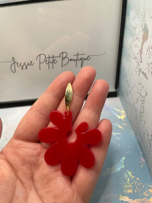 Red flower-shaped earring held in a hand with a blurred background