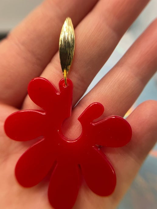 Red flower-shaped object with a gold center held in a hand against a blurred background