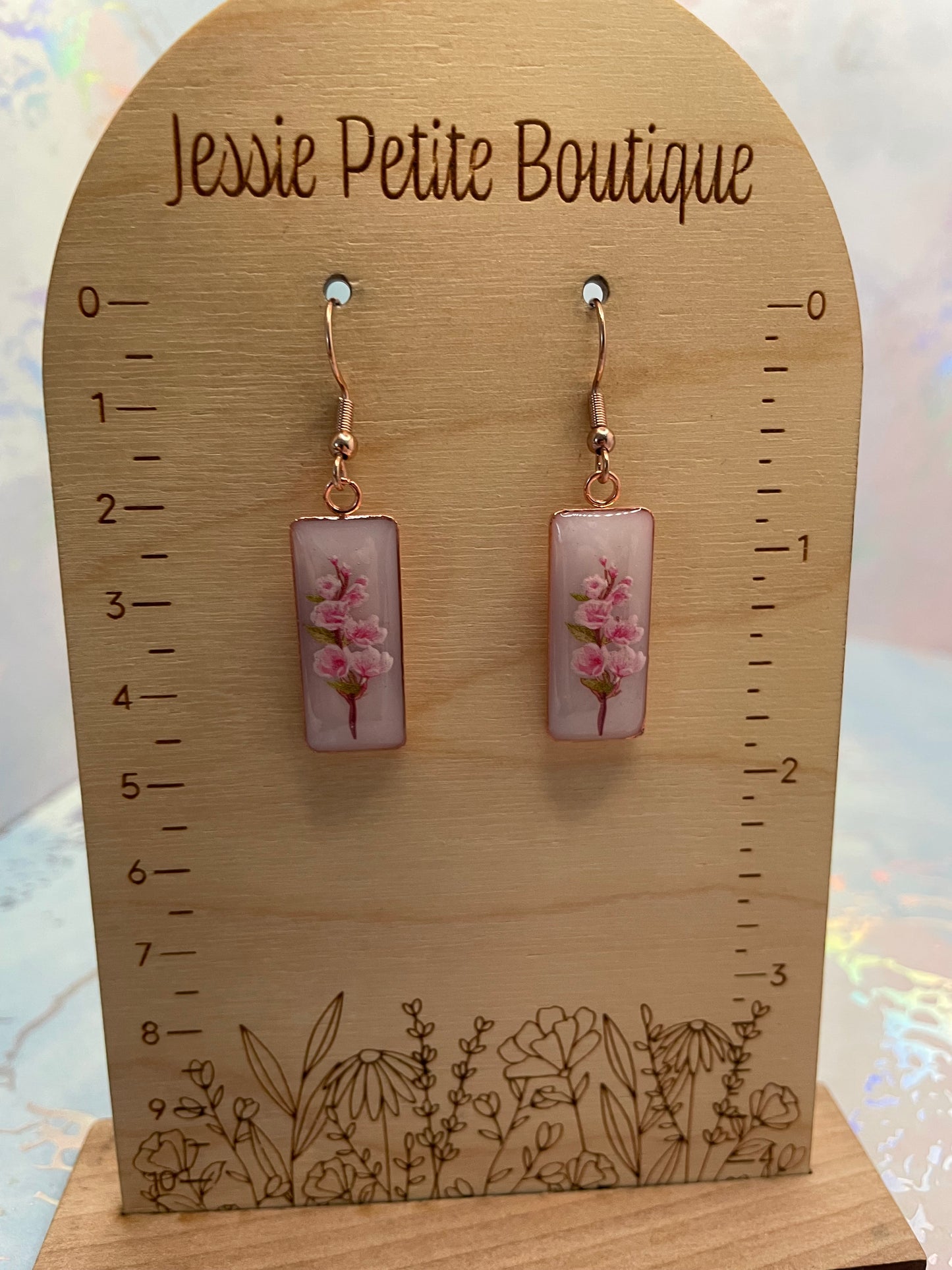 Pair of earrings on a wooden card with floral design, labeled 'Jessie Petite Boutique'.