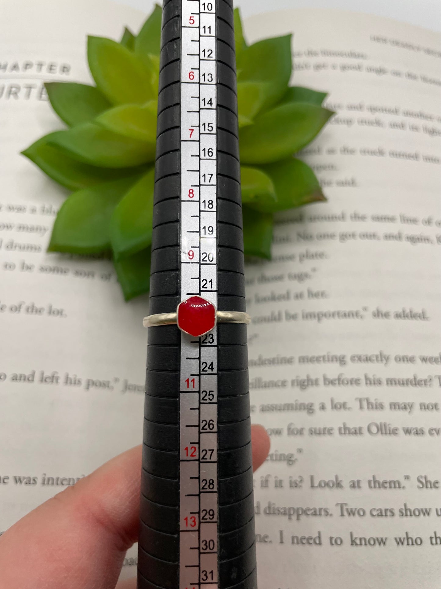 Ring with a red stone held against a ruler on a book page