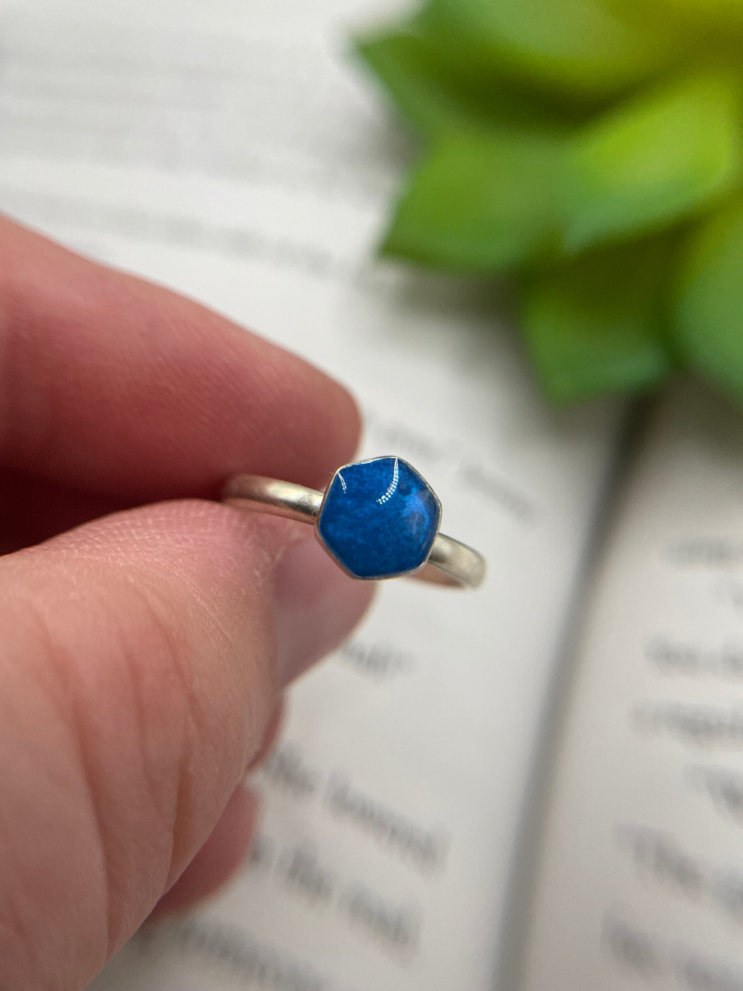 Hand holding a silver ring with a blue stone against a blurred background