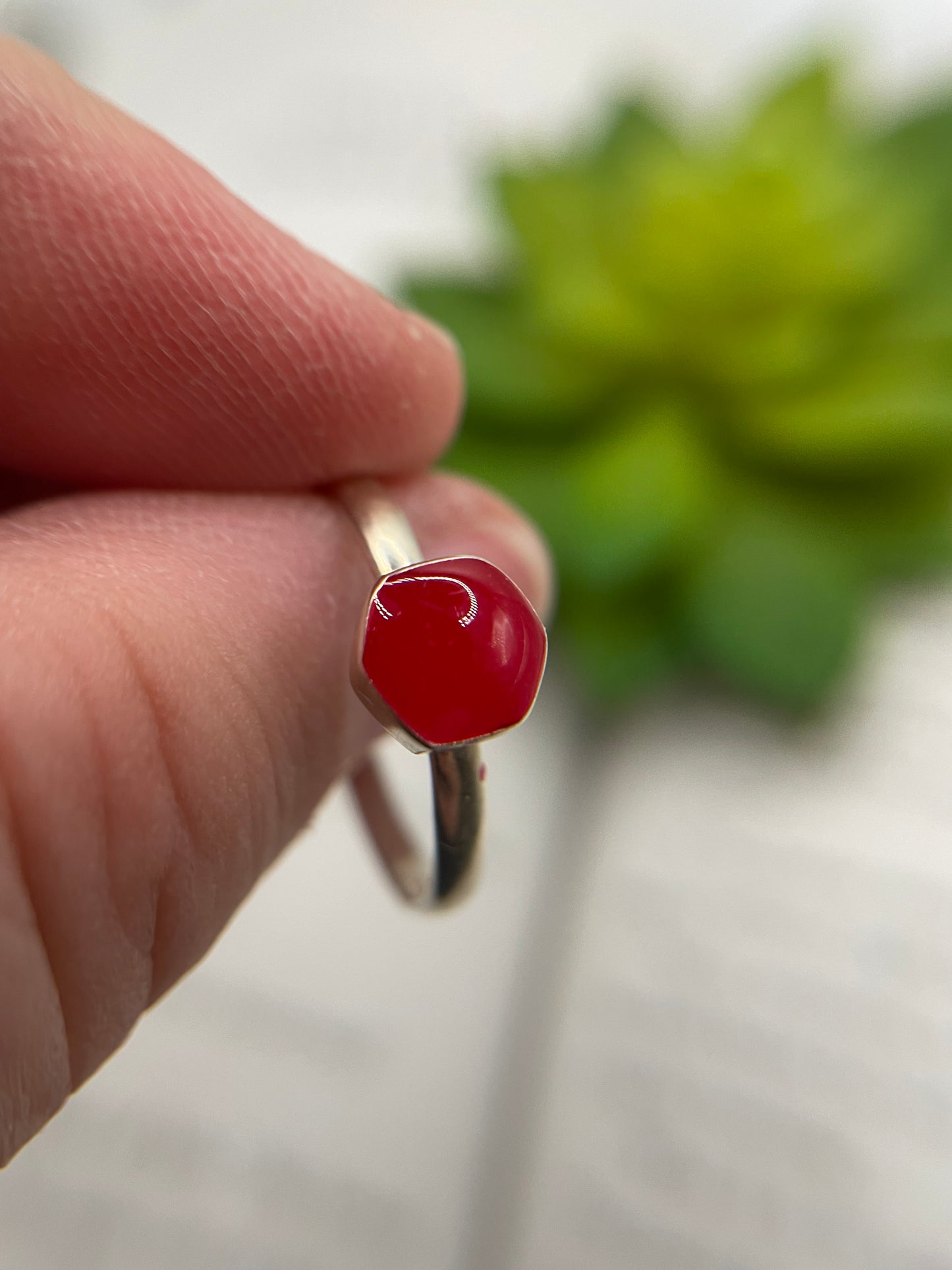 Silver ring with a red stone held between fingers against a blurred green plant background