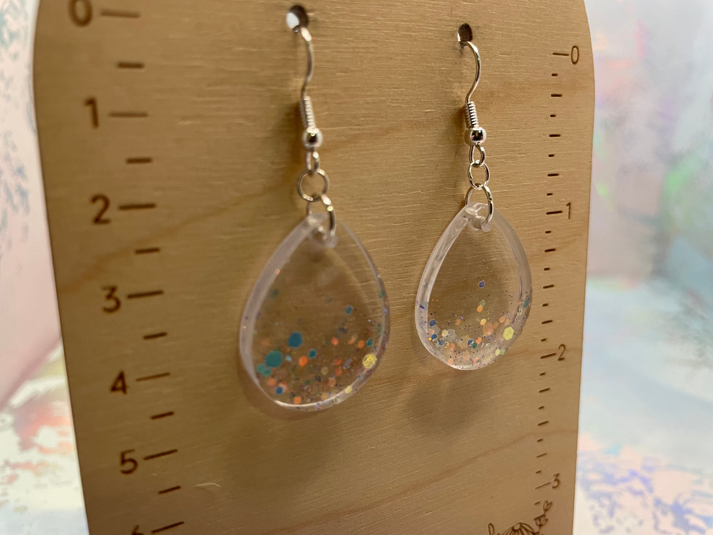 Teardrop-shaped earrings with glittery interior on a wooden ruler background