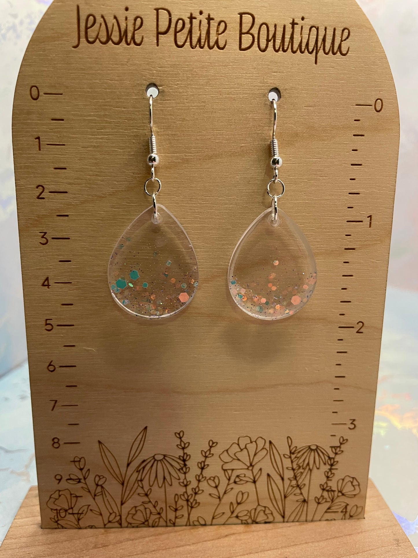 Clear earrings  on a wooden card with measurements and floral design, branded 'Jessie Petite Boutique'.