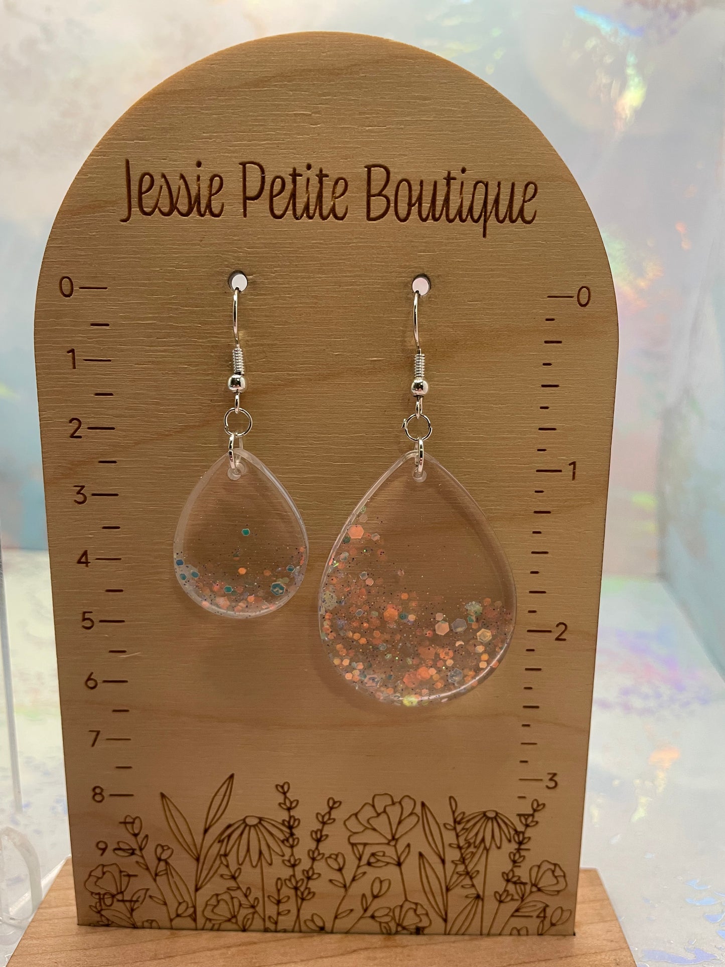 Wooden earring display card with floral design and 'Jessie Petite Boutique' text, featuring clear earrings with glitter.