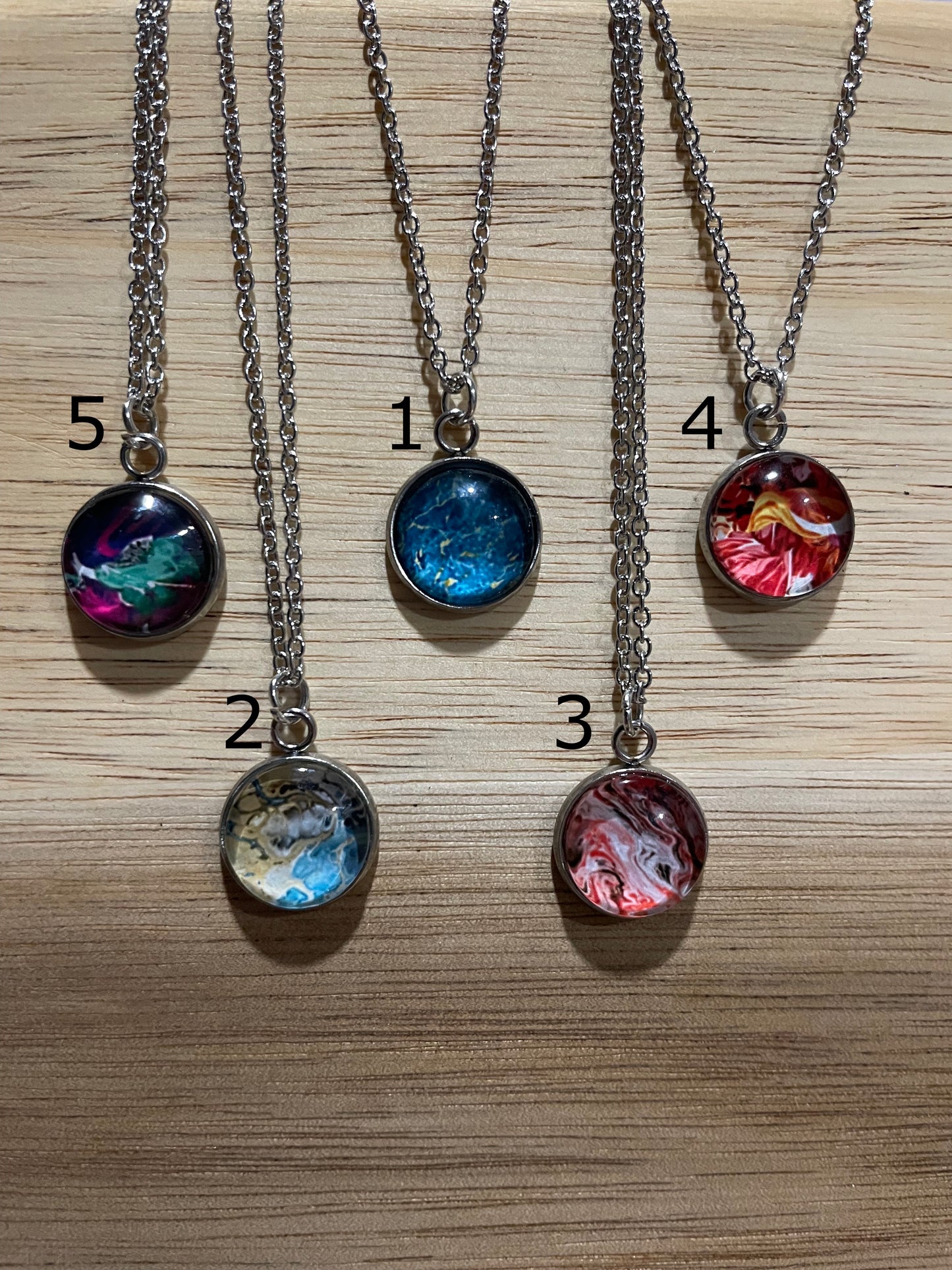 Four necklaces with colorful pendant designs on a wooden surface