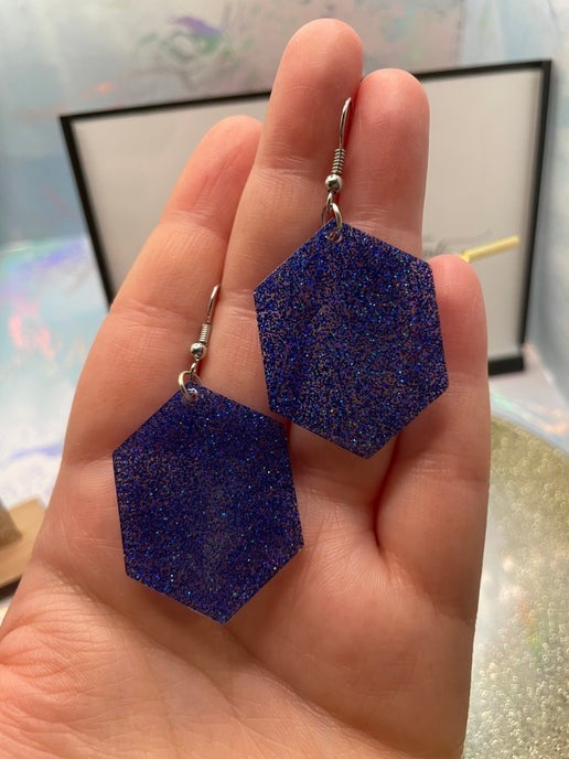 Blue glittery earrings held in a hand with a blurred background