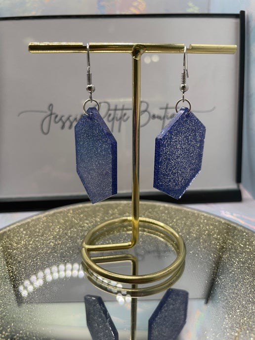 sparkly blue hexagon earrings on a gold display stand with a blurred background