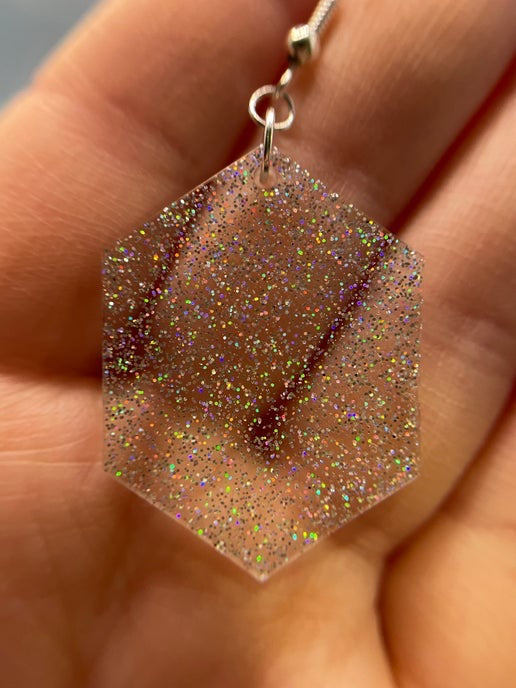 Hexagonal glittery earring held in a hand