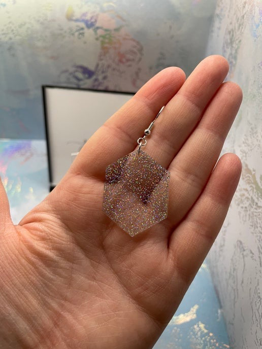 Hand holding a clear glittery earring with a colorful abstract painting in the background