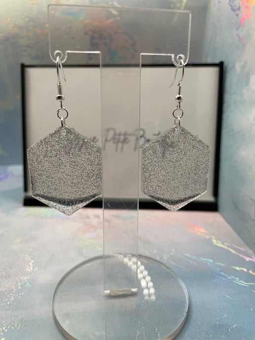 Silver glittery geometric earrings on a clear stand with a colorful background