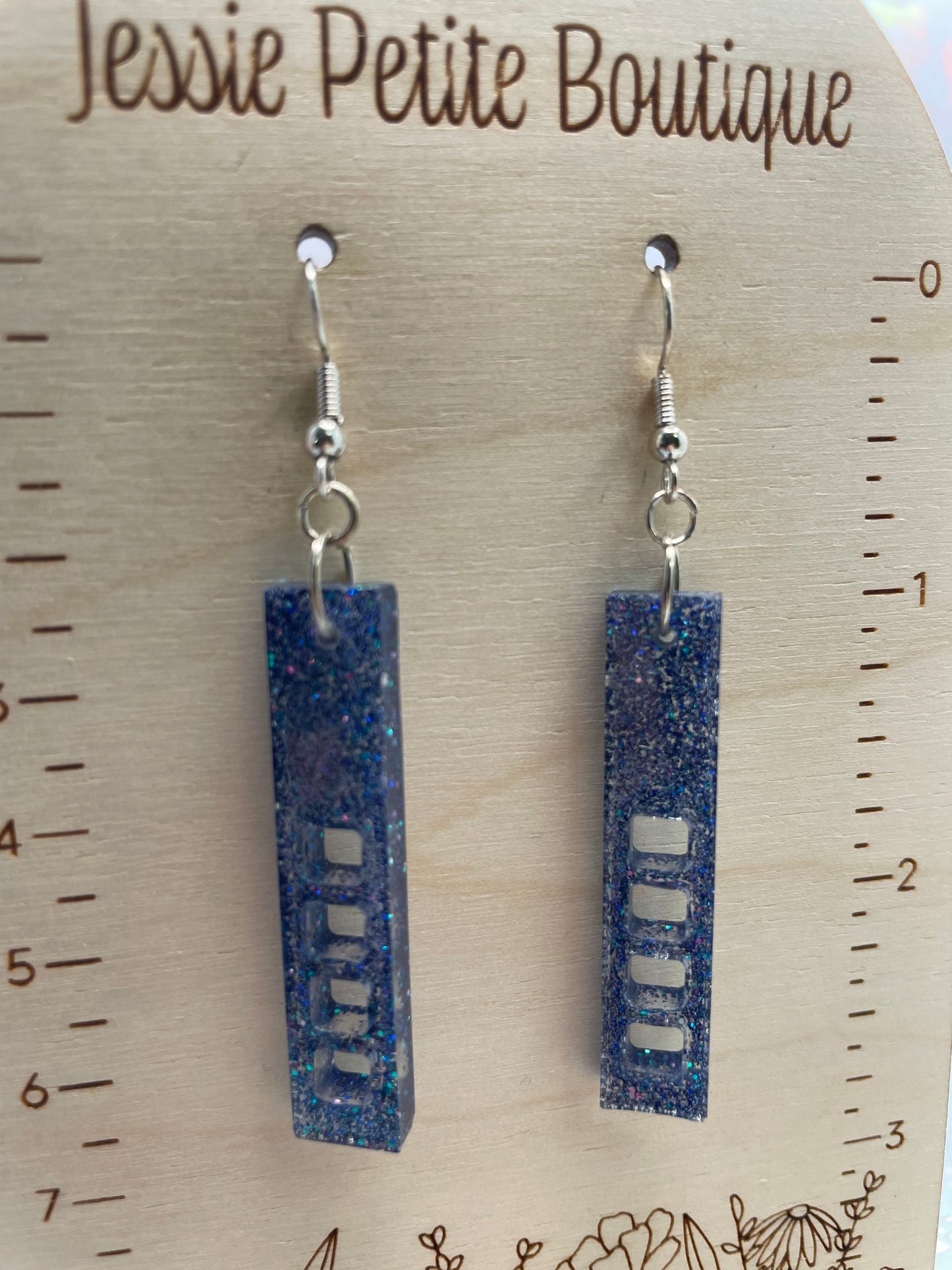 sparkly purple:skyscraper earrings on a wooden stand with a ruler for scale.