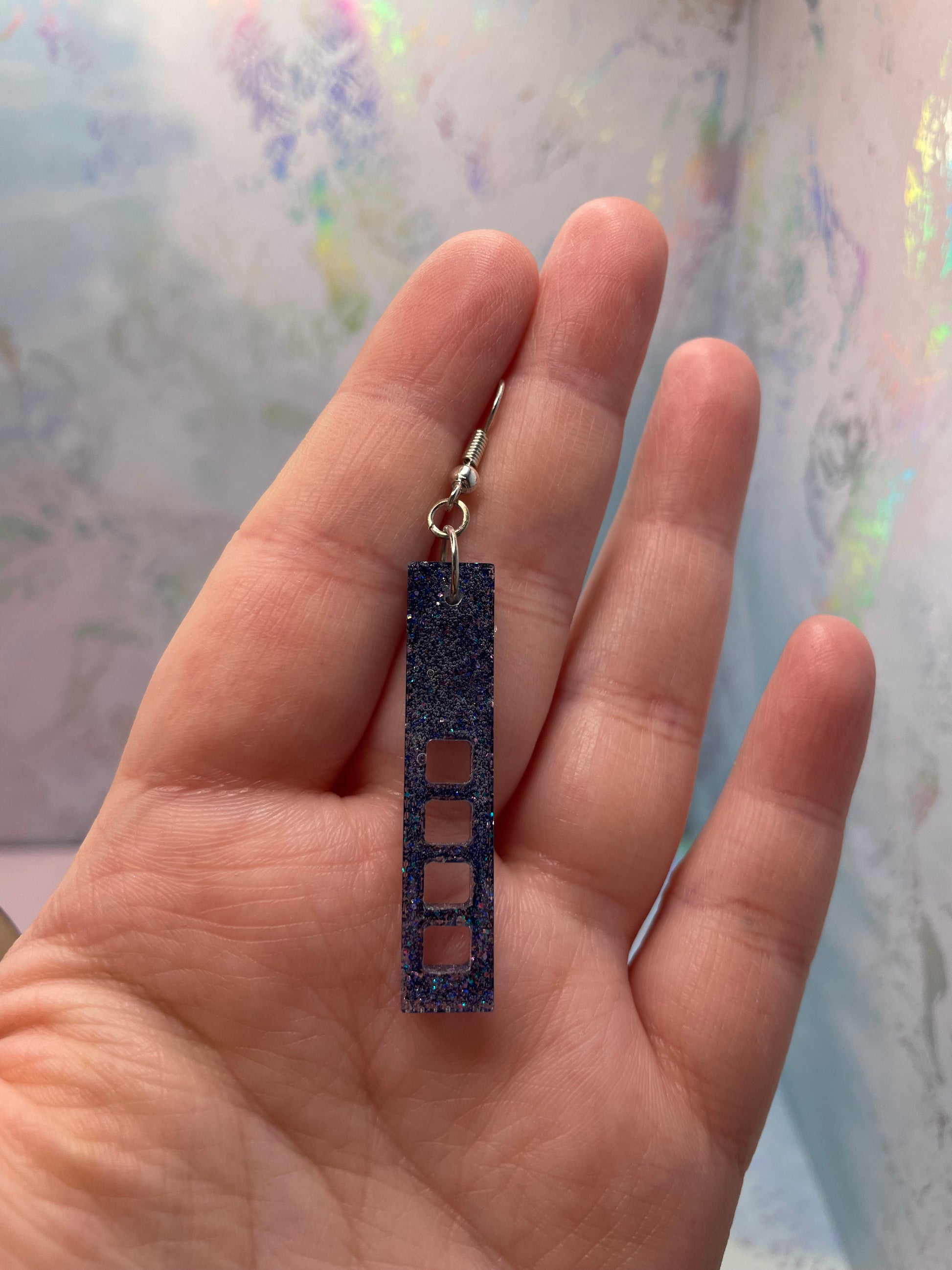 Hand holding a sparkly purple:skyscraper earrings against a patterned background