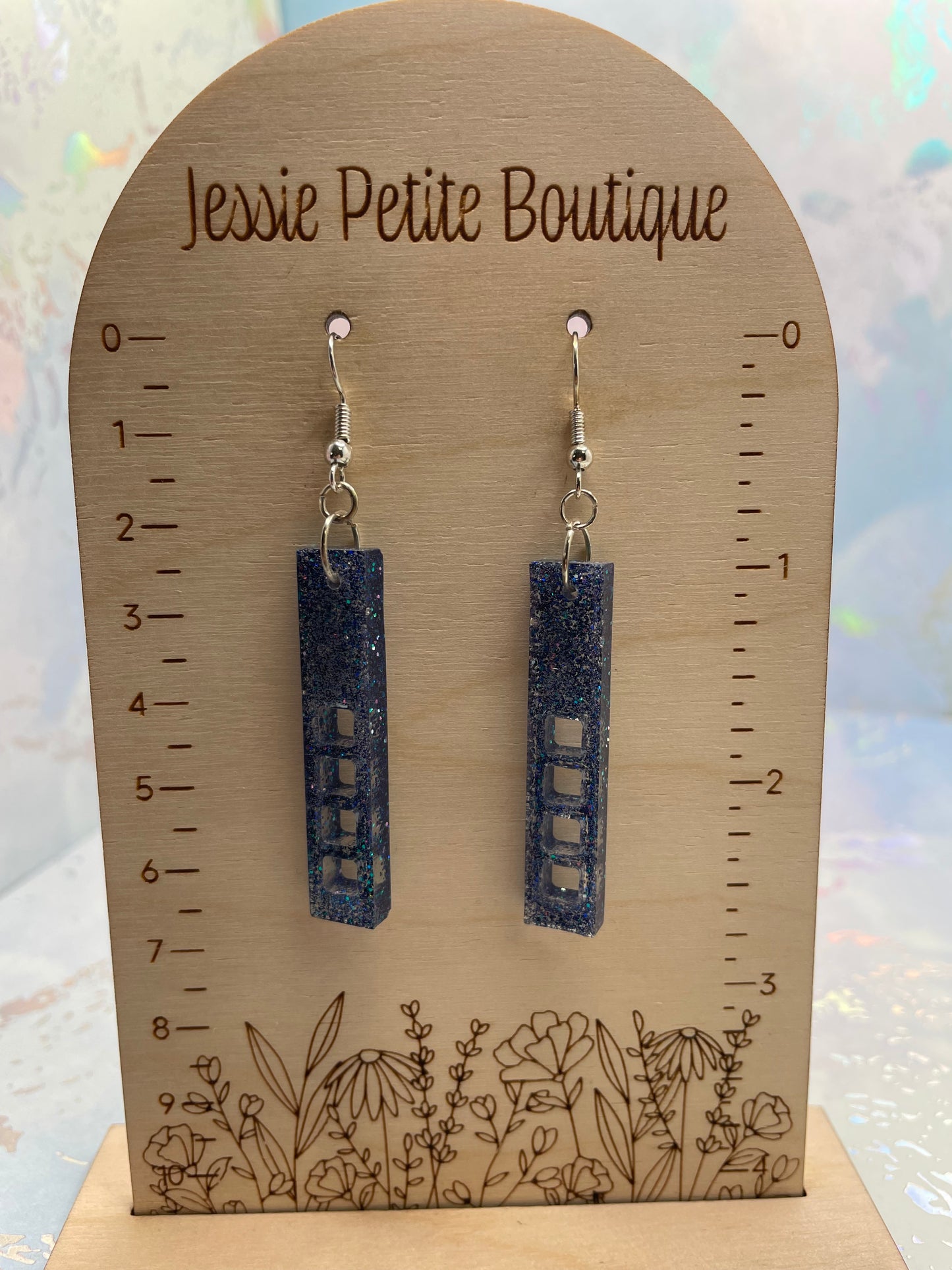 sparkly purple rectangular earrings on a wooden display card with measurements and floral design, branded 'Jessie Petite Boutique'.