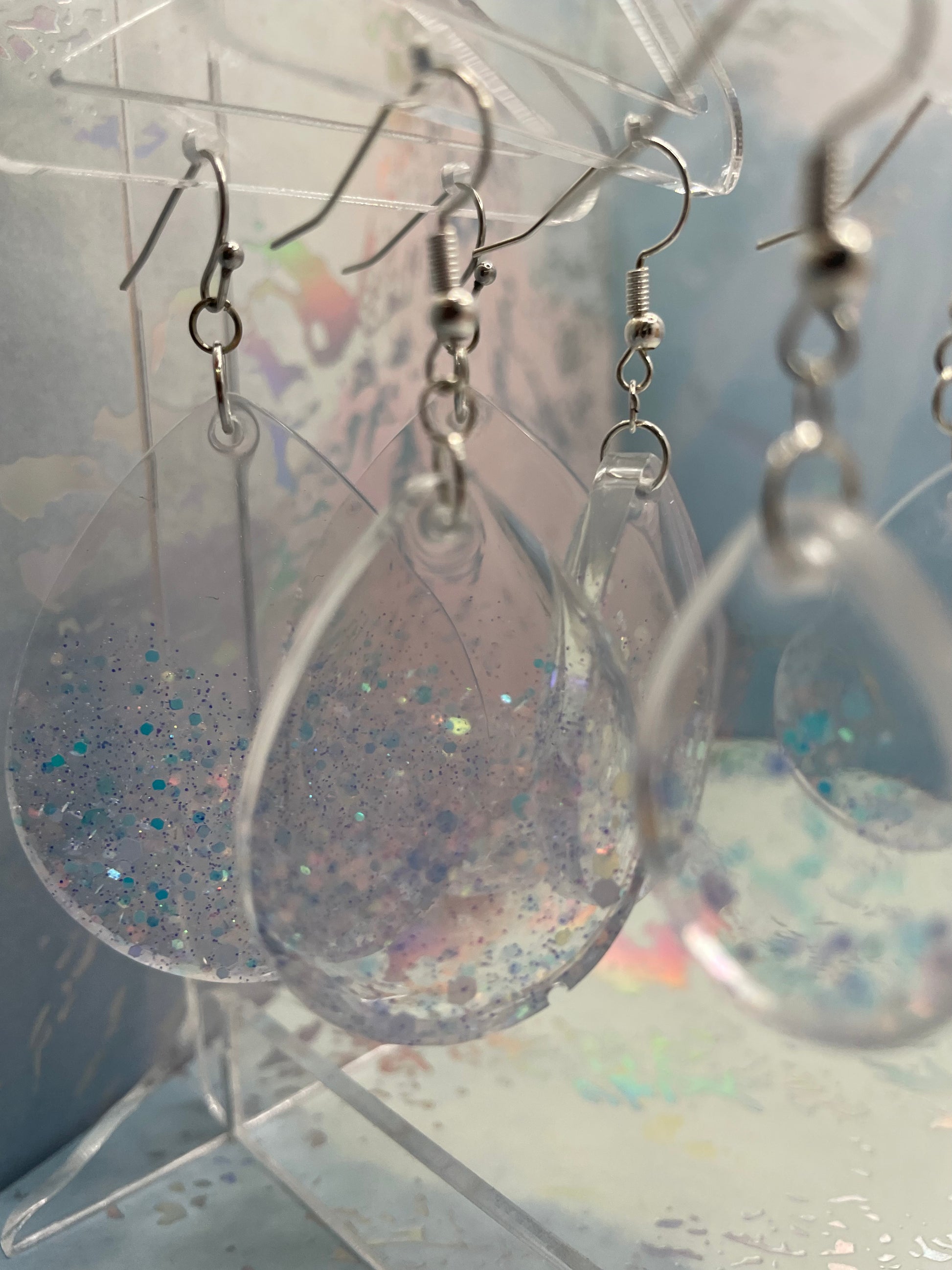 Sparkly teardrop shaped earrings on a clear stand with a colourful background