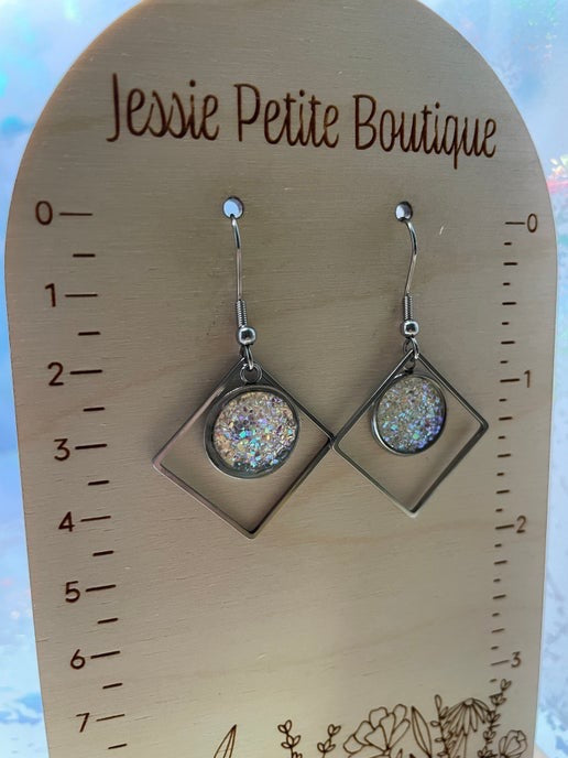 Silver earrings with a glittery center on a wooden card labeled 'Jessie Petite Boutique'.