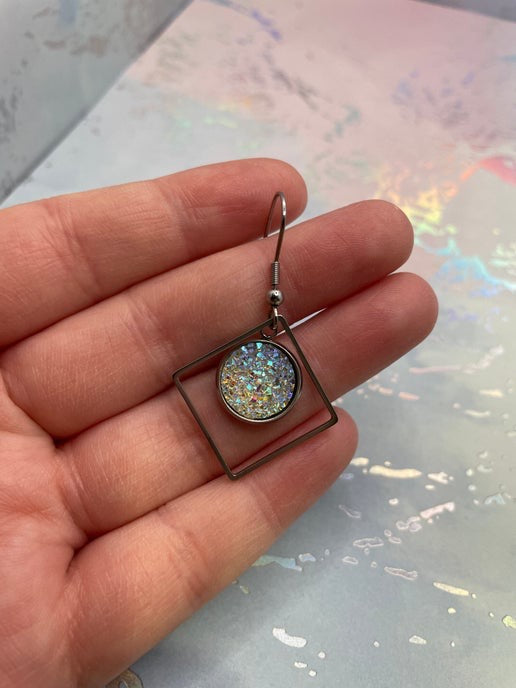 Earring with a glittery center held between fingers against a reflective surface