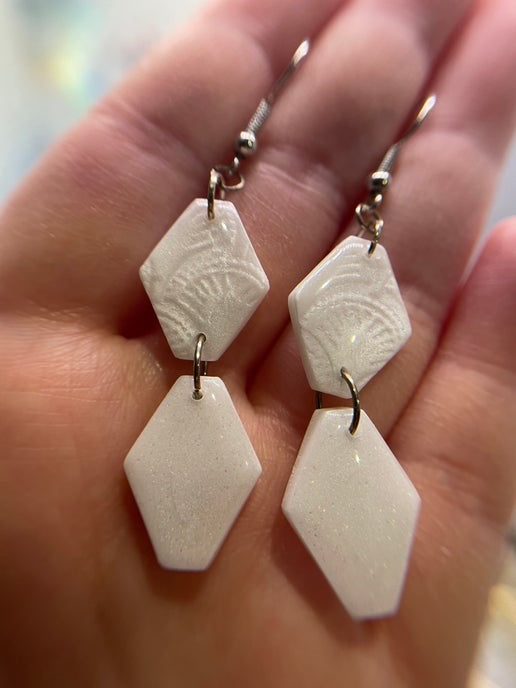 White geometric earrings held in a hand with a blurred background