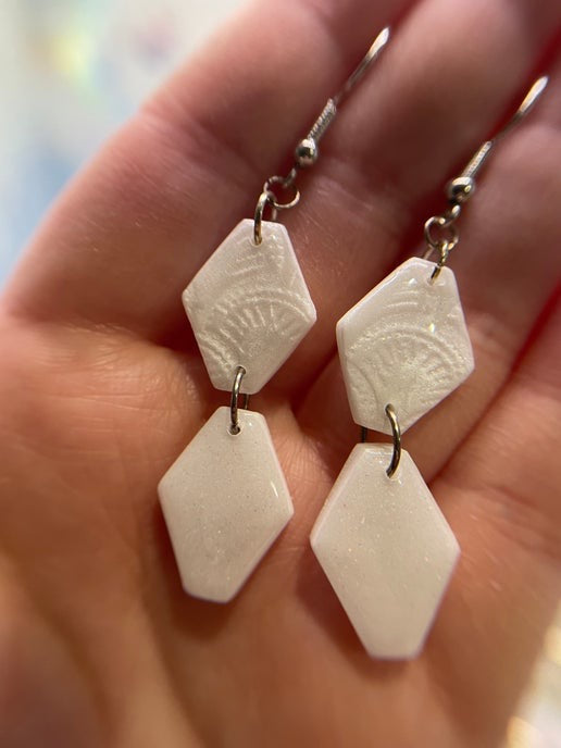 White geometric earrings held in a hand with a blurred background