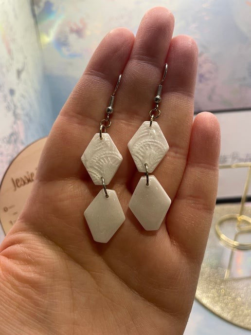 White geometric earrings held in a hand with a blurred background
