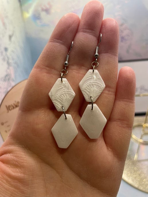 White geometric earrings held in a hand with a blurred background