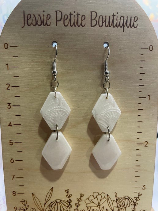 Pair of white geometric earrings on a wooden display card with 'Jessie Petite Boutique' branding.