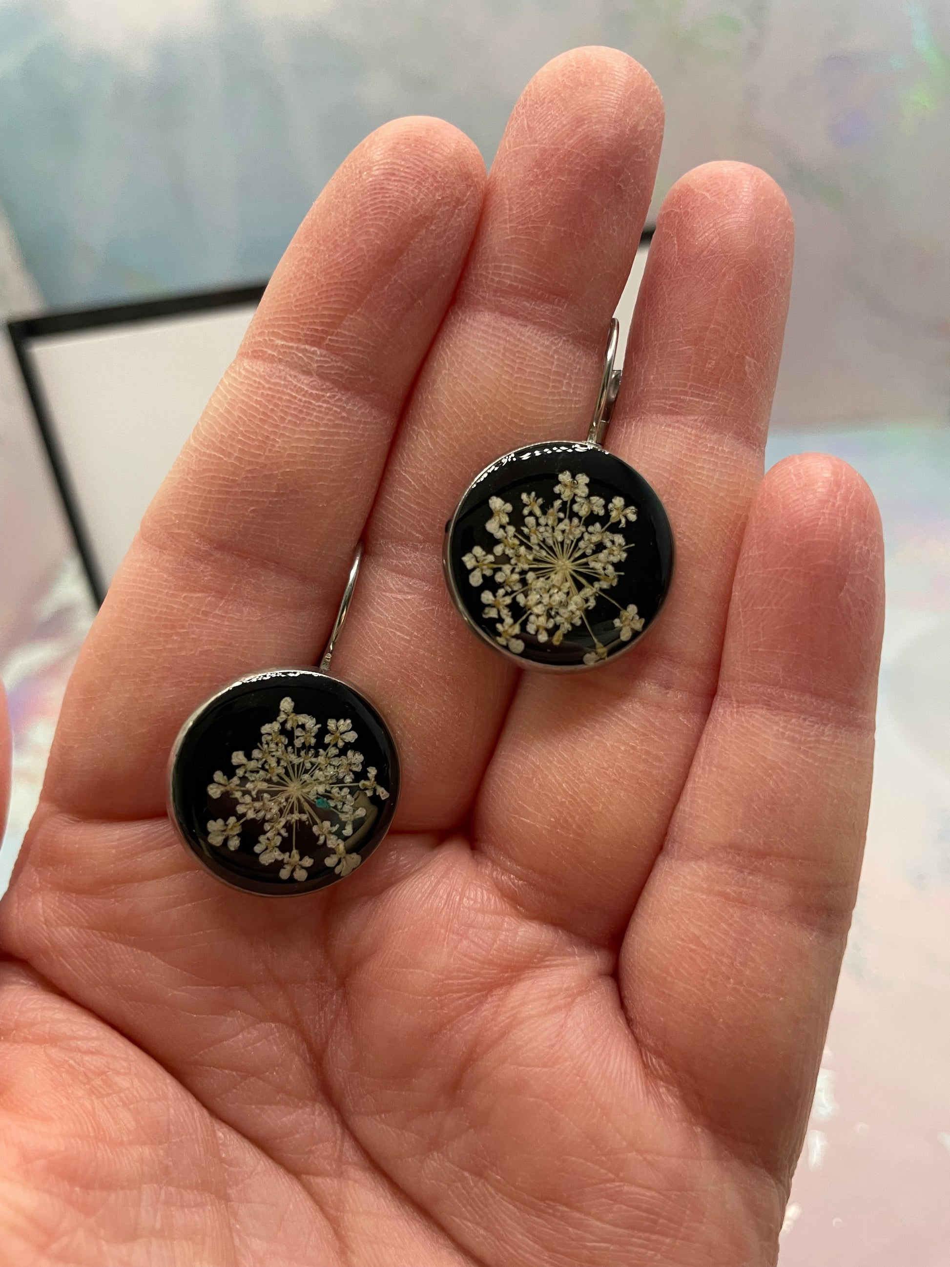 Round earrings with floral design held in a hand against a blurred background