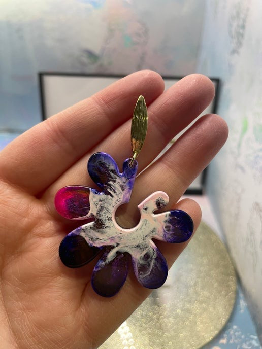 Colorful flower-shaped earring held in a hand with a blurred background
